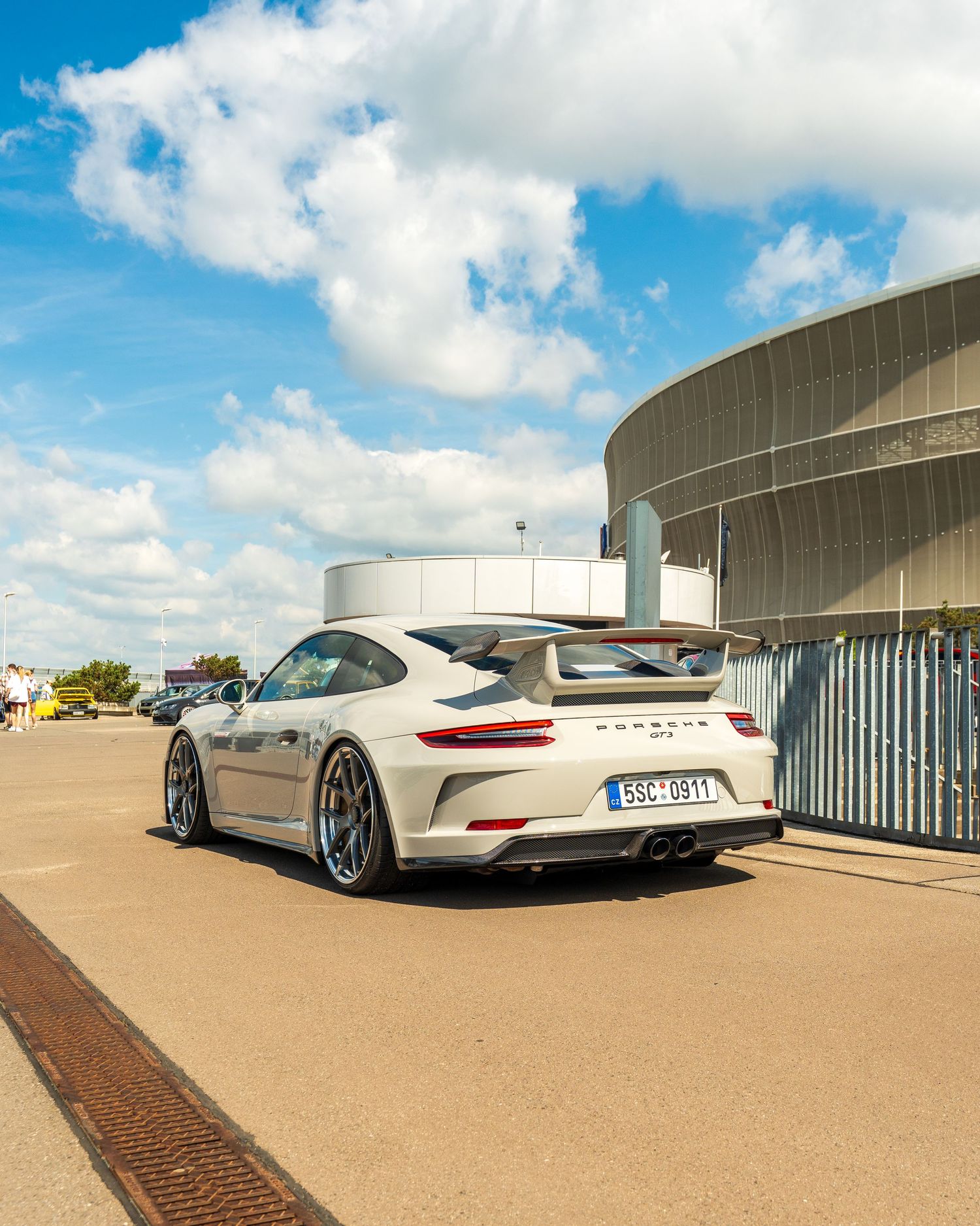 Multiple luxury sports cars parked on a rooftop terrace under blue skies with white fluffy clouds.