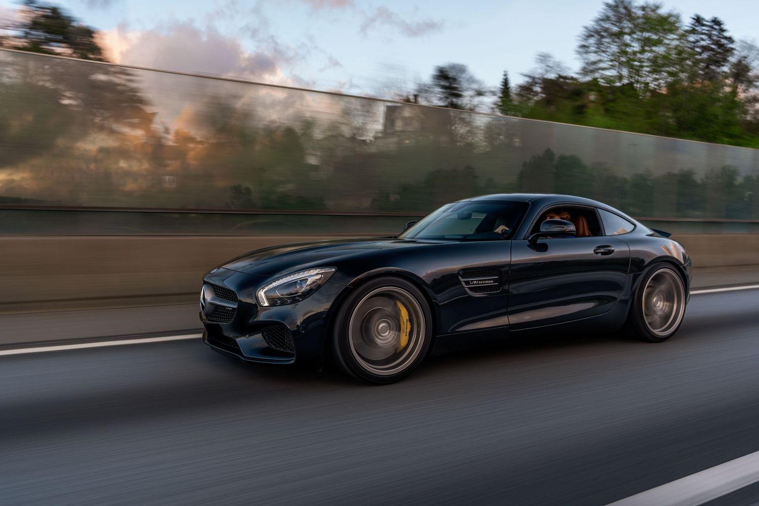 Dark Mercedes-AMG GT speeds past concrete barrier with dramatic motion blur effect.