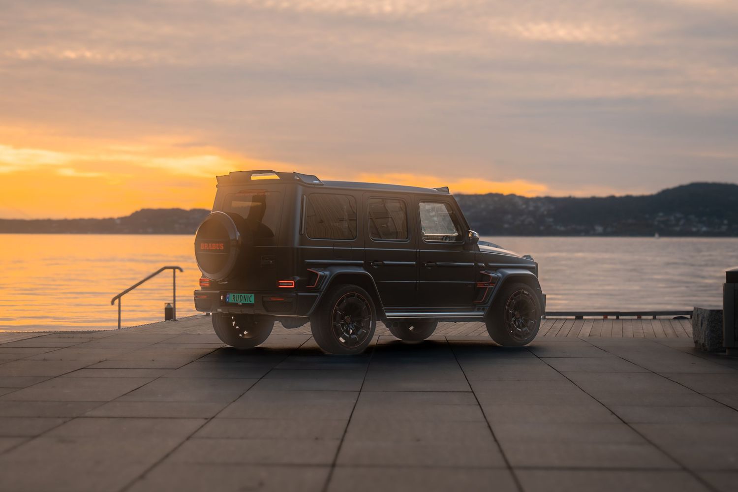 Silhouette of a truck parked near a beach during a vibrant golden sunset with calm ocean waters in the background.