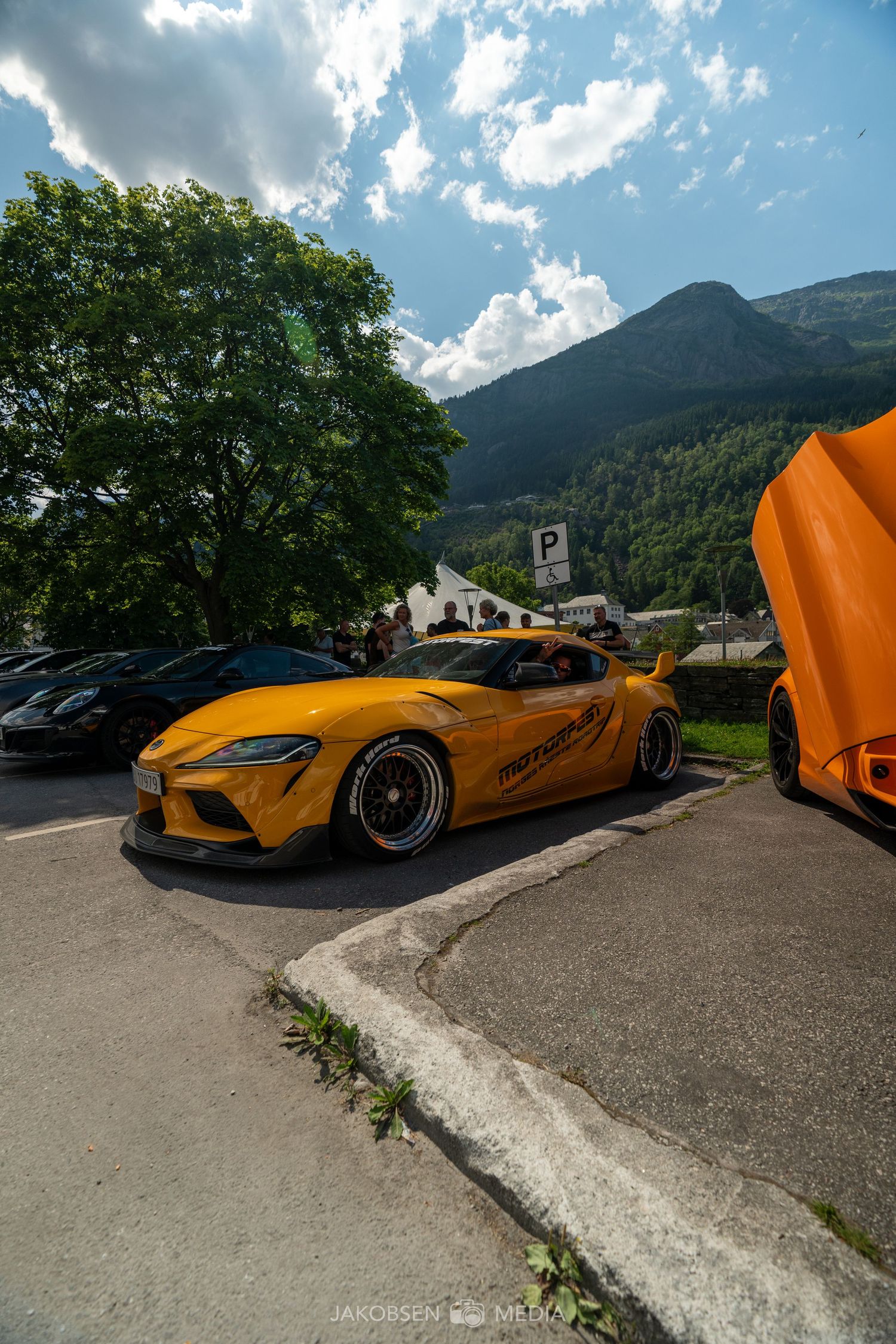 Orange McLaren supercar with butterfly doors open parked in a mountain setting with scenic views.