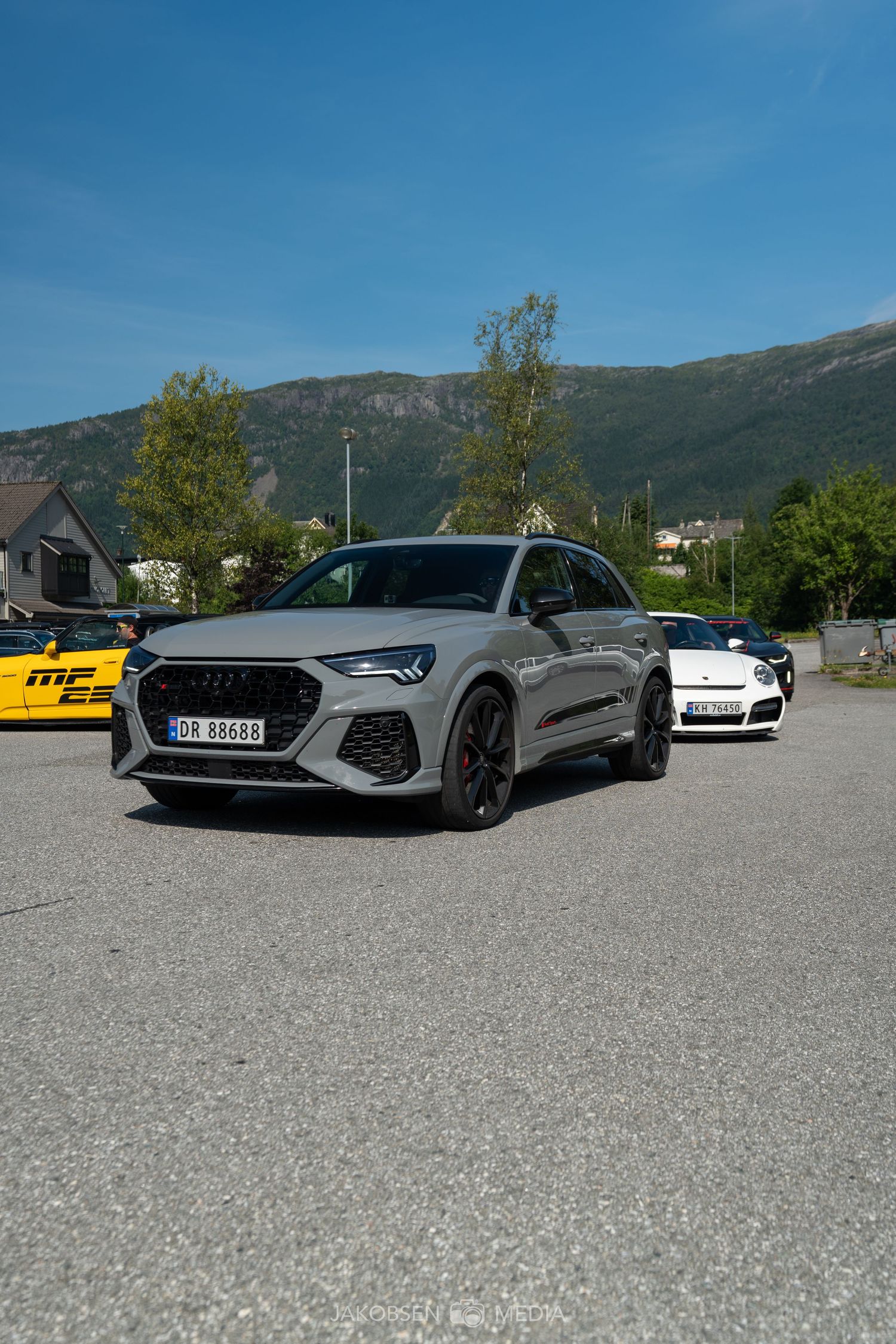 Line of luxury sports cars parked in a gravel lot with mountains in the background.
