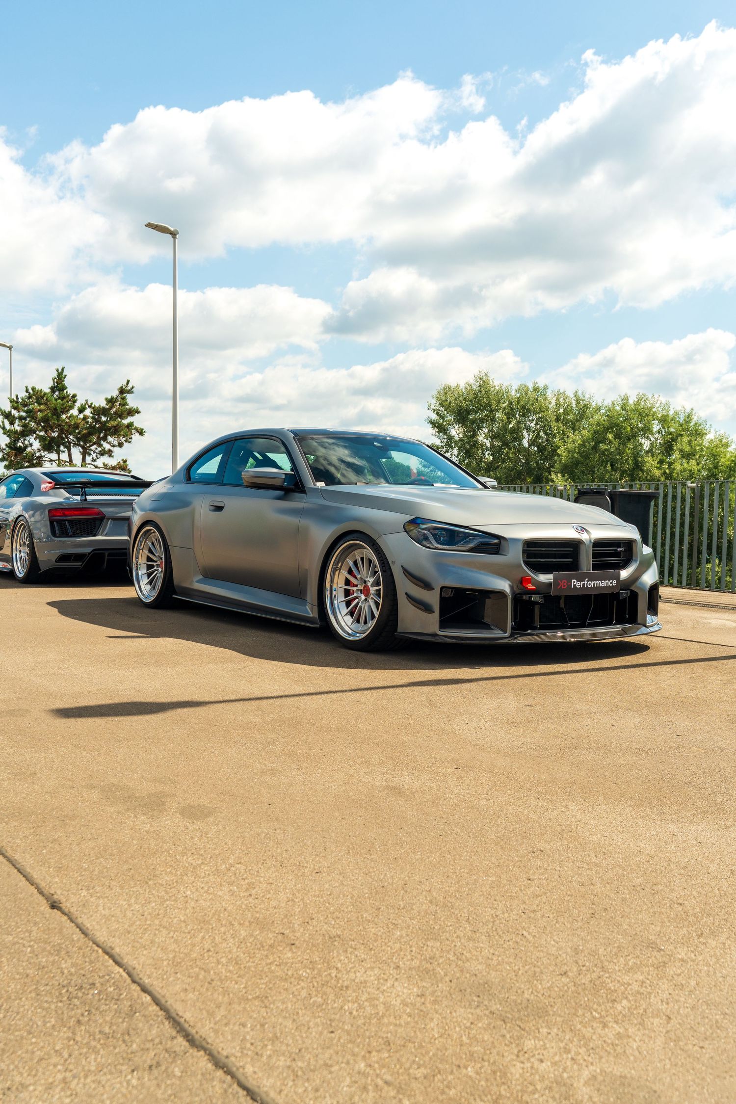 Modified gray BMW M4 with lowered suspension and custom wheels parked on a sunny day.