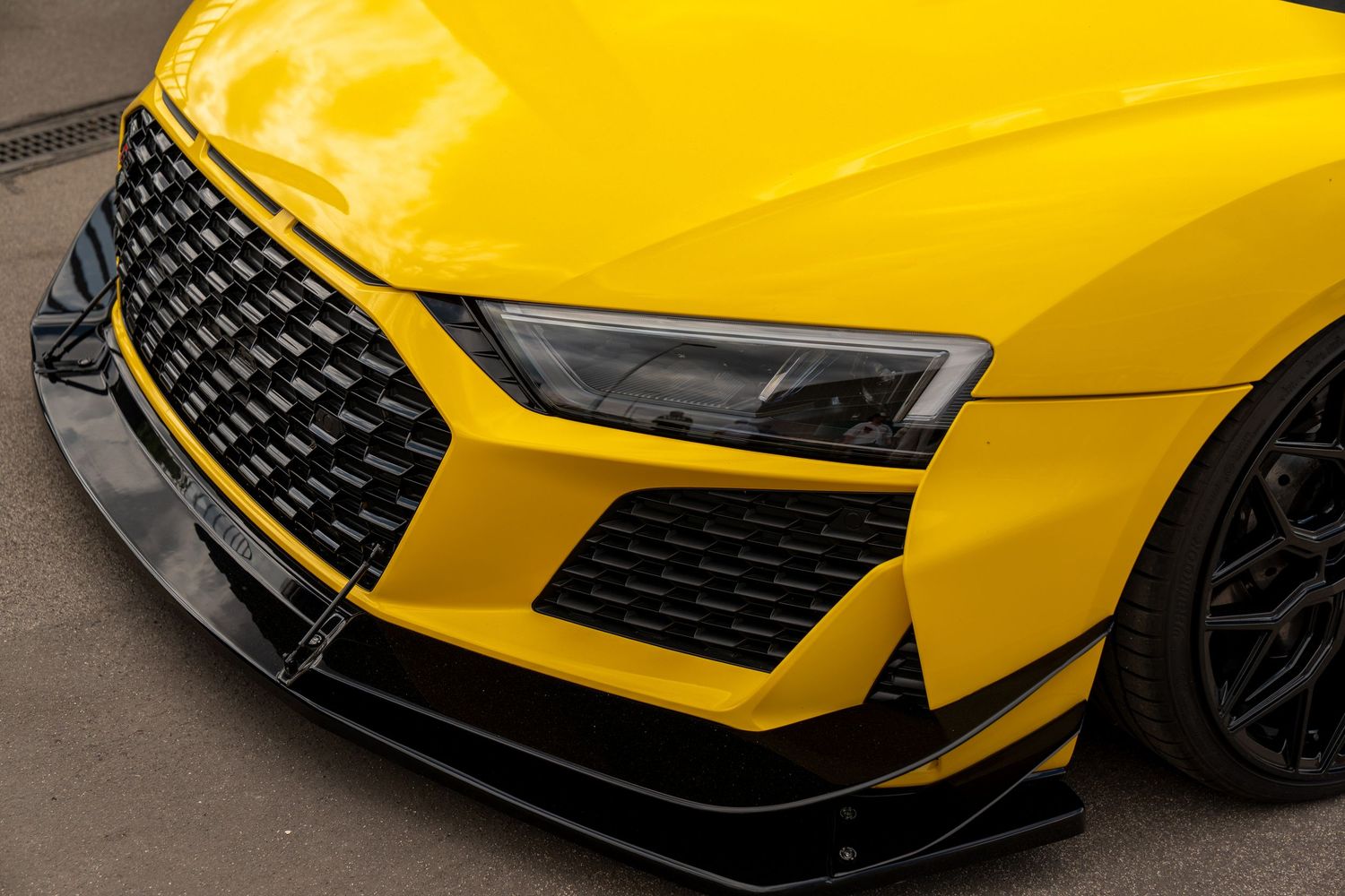 Close-up of bright yellow Audi R8 front bumper with custom carbon fiber splitter and grille.
