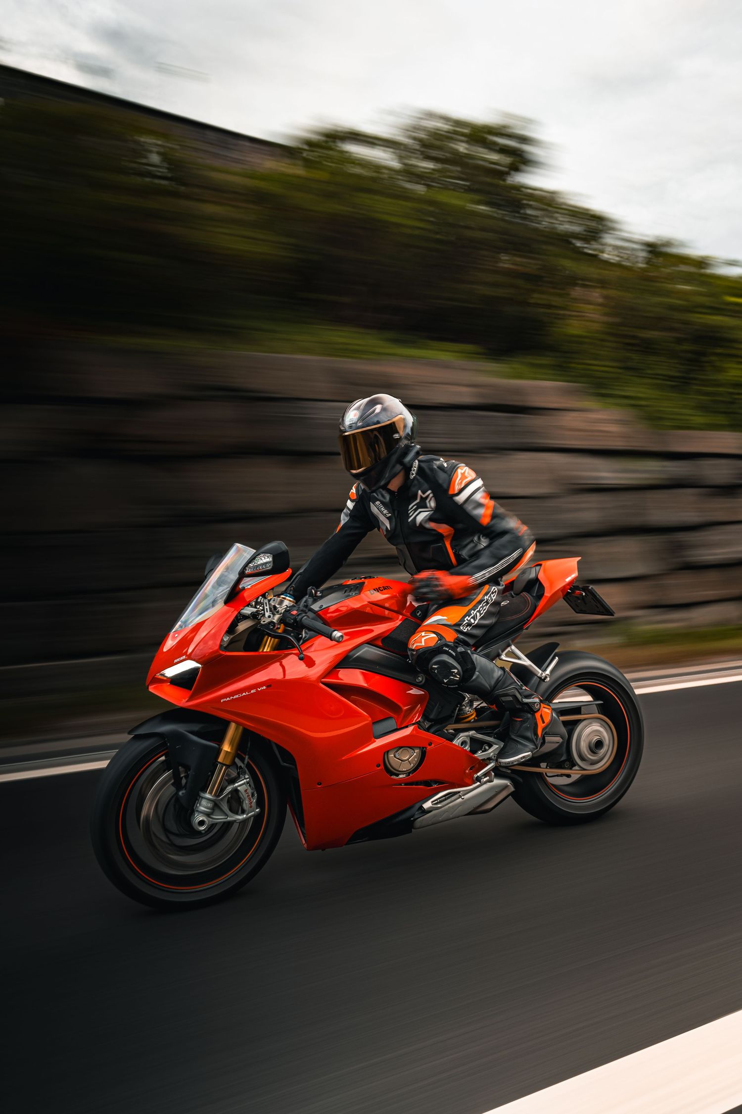 A motorcyclist rides a bright red sports bike at high speed on a blurred motion background.