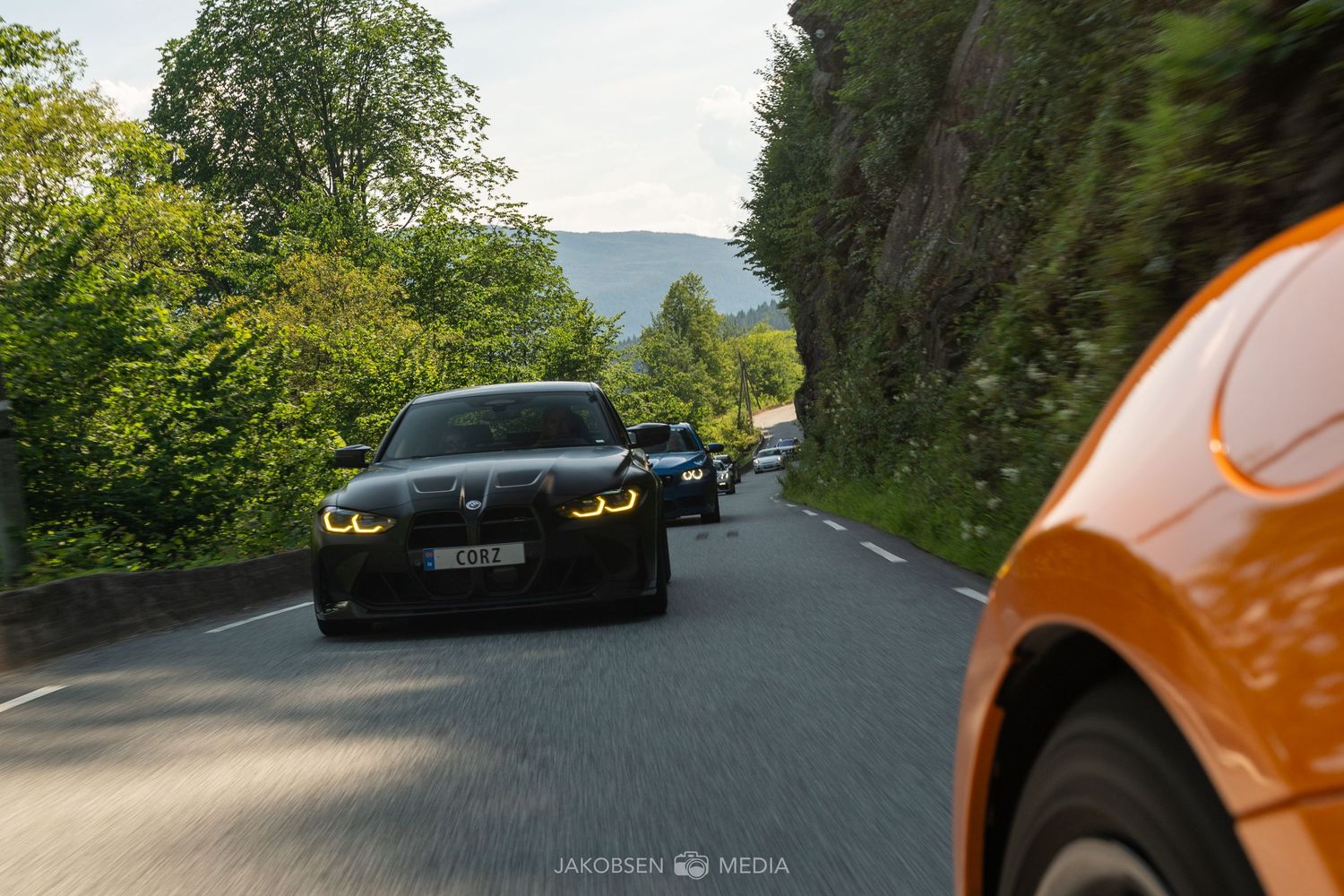 Sports cars driving on a winding forest road with trees lining both sides.