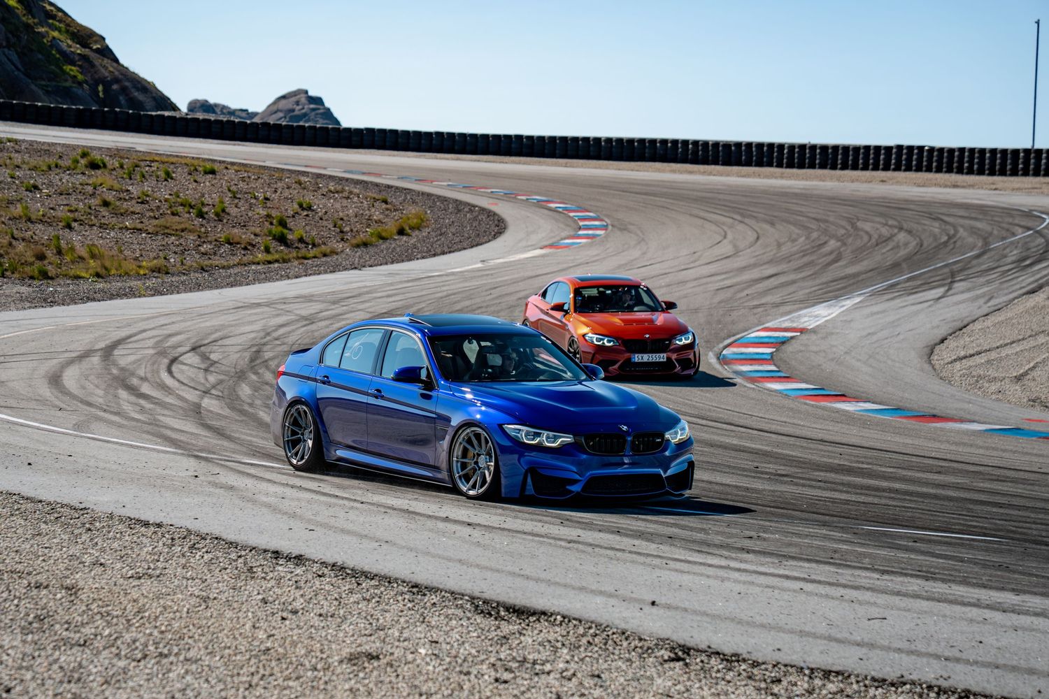 A blue BMW M4 sports car drifts around a winding racetrack with tire marks visible on the asphalt surface.