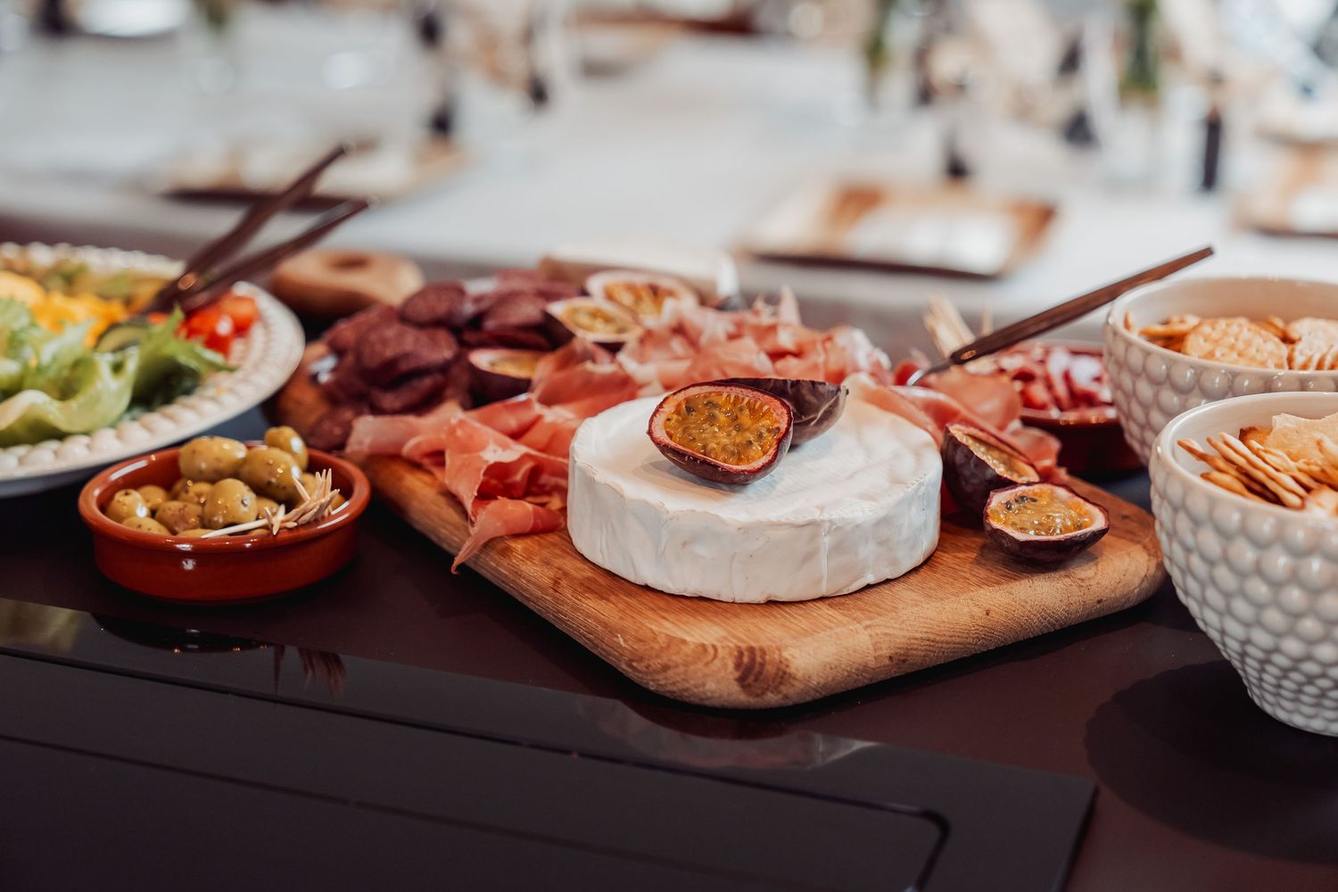 A charcuterie board with brie cheese, cured meats, figs, crackers, and olives on a wooden cutting board.