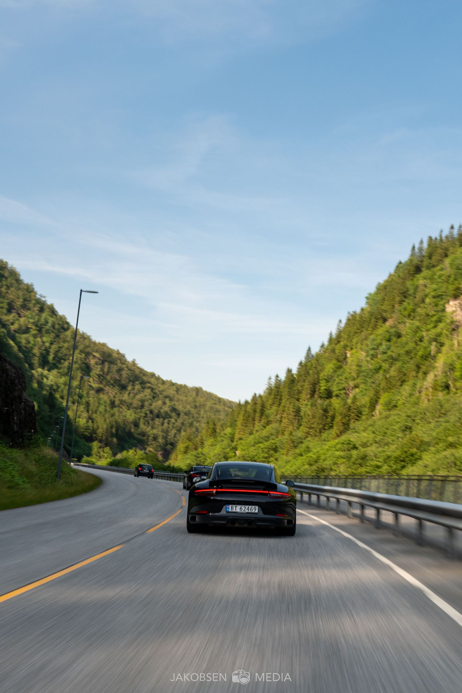 Black sports cars cruising along a winding mountain highway surrounded by lush forest views.