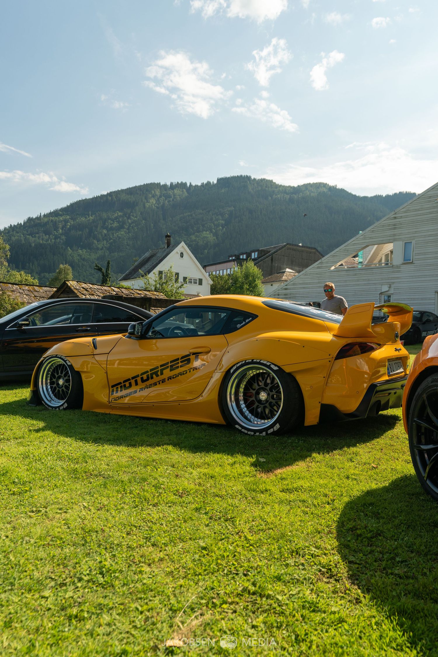 Yellow and white custom sports cars on display at an outdoor car show with mountains visible.