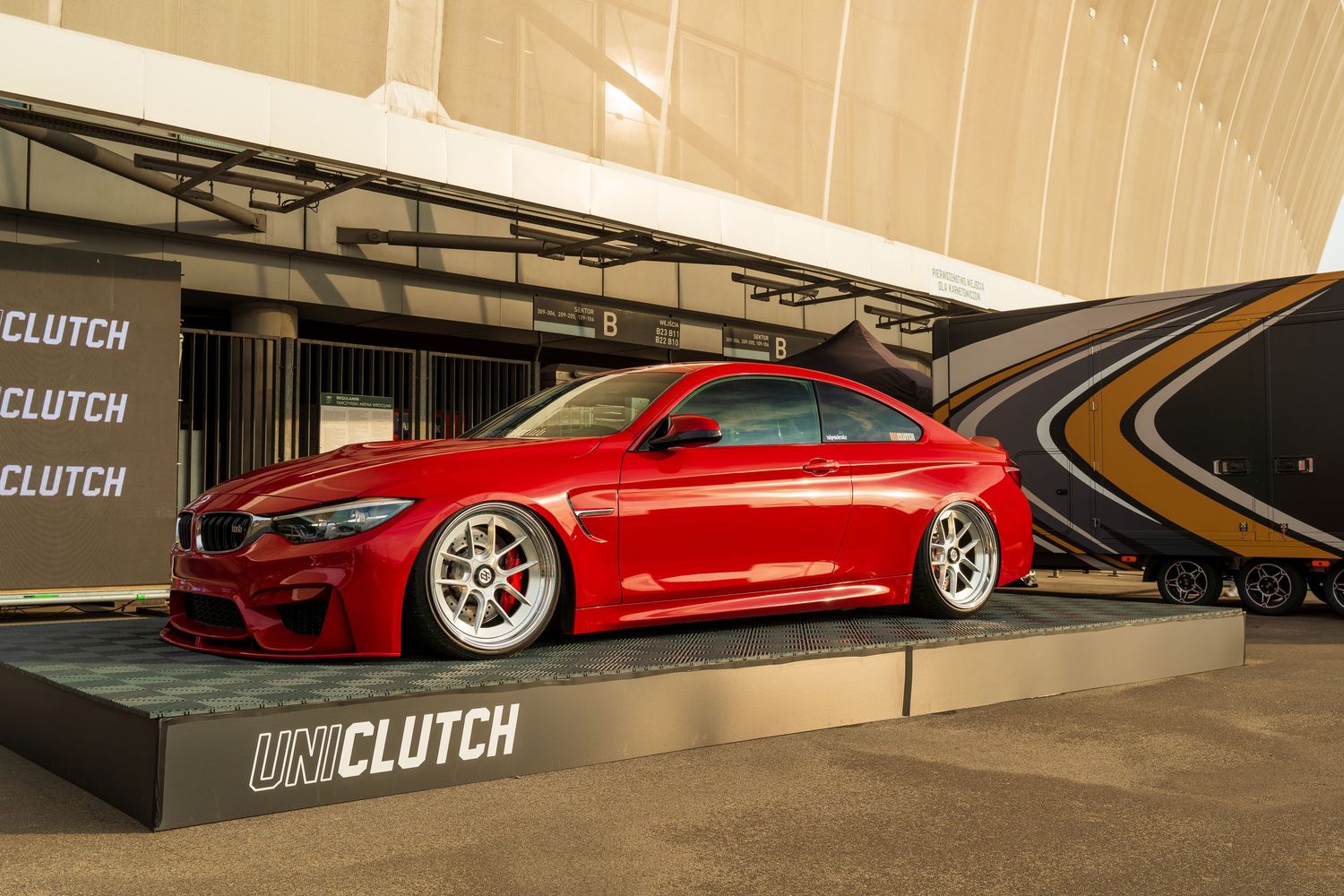Red luxury sports car with custom wheels displayed on a platform in front of a Clutch branded wall.