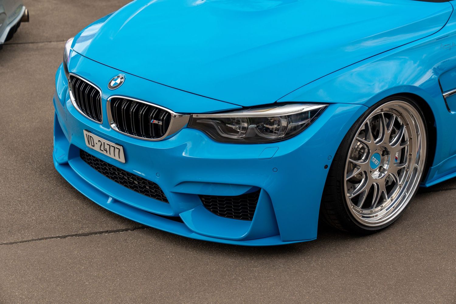 Close-up front quarter view of modified blue BMW M3 with custom mesh wheels.