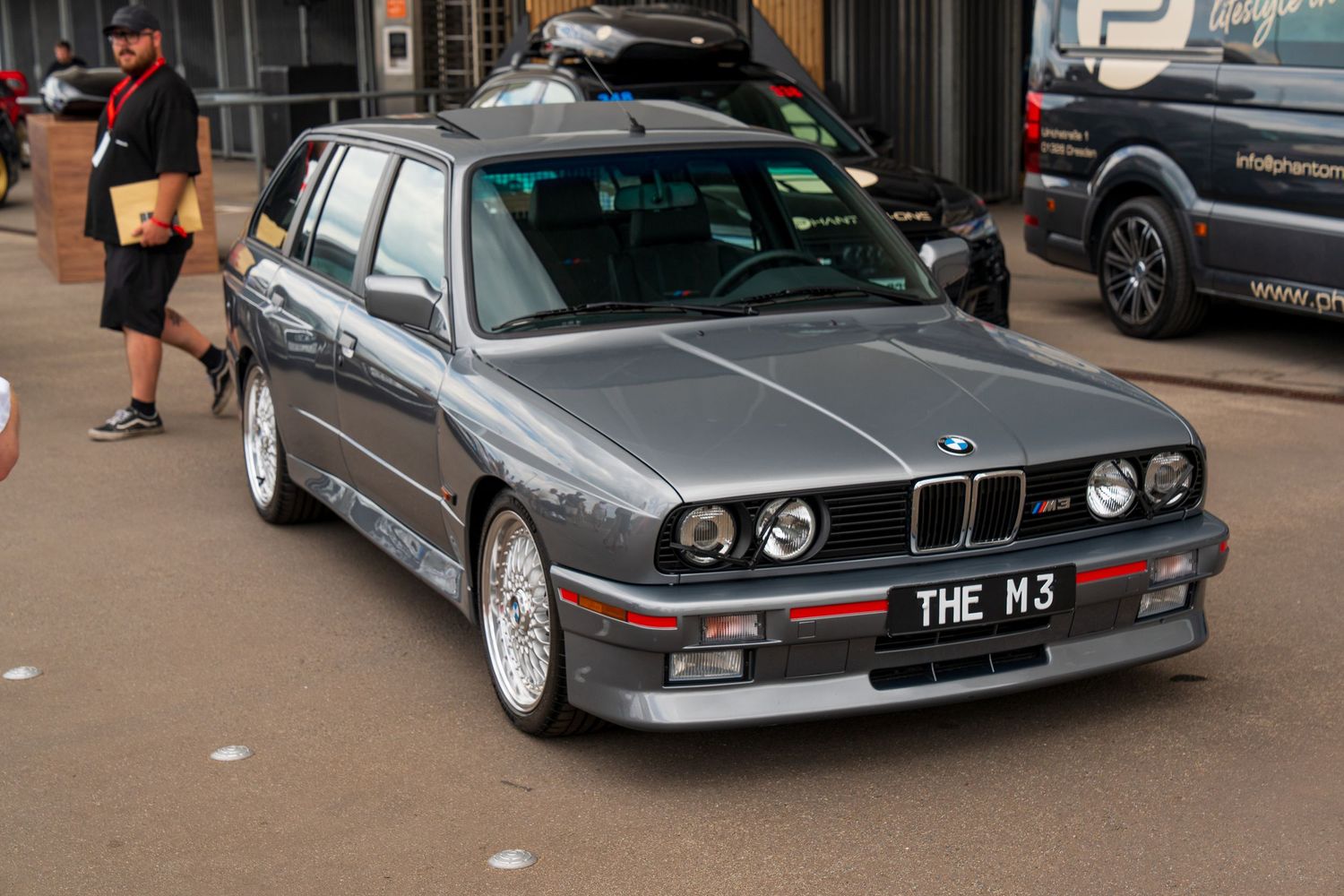 A classic BMW M3 E30 wagon in silver with BBS wheels parked at an automotive event.