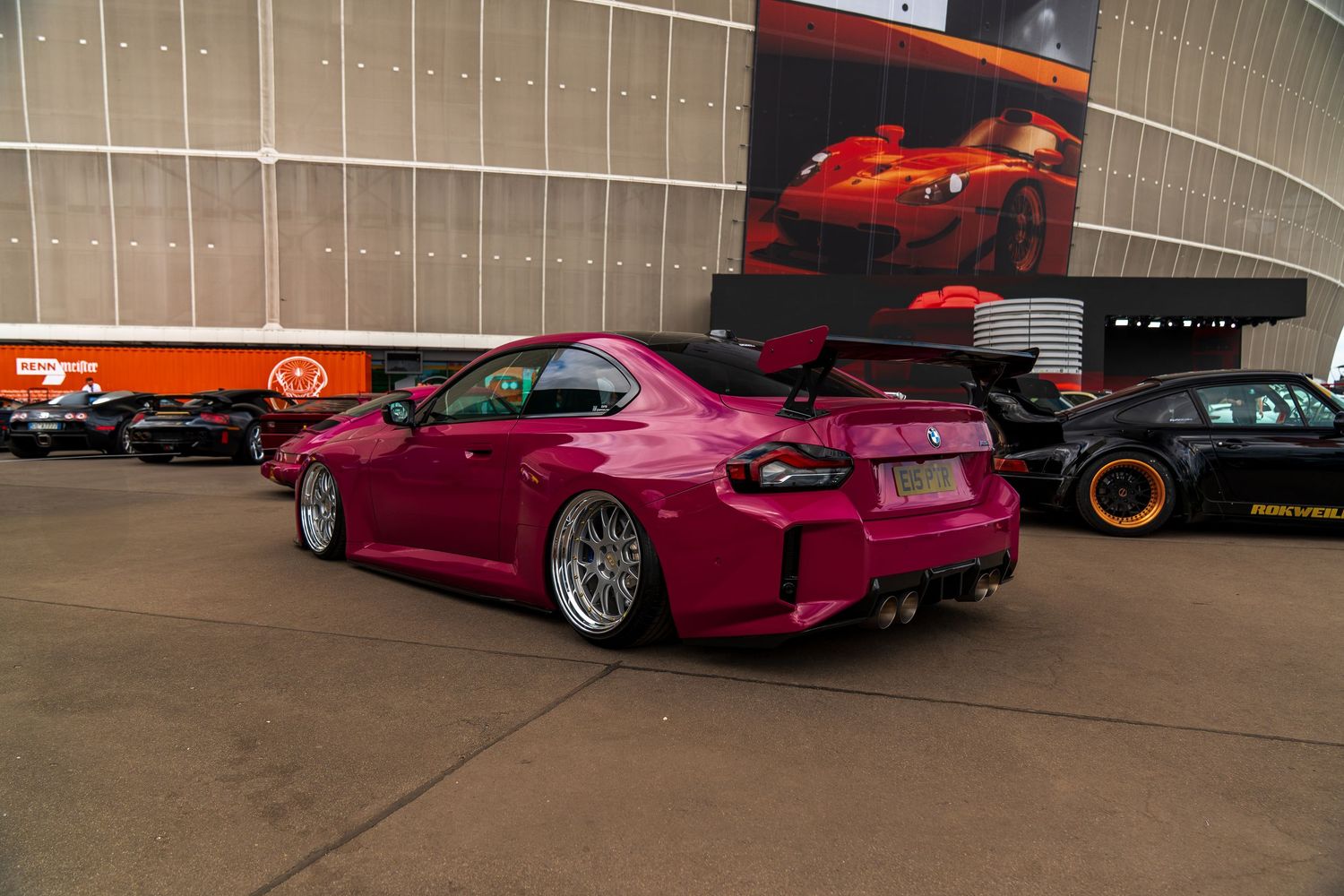 Modified pink Toyota showing a widebody kit and custom wheels at an automotive event.