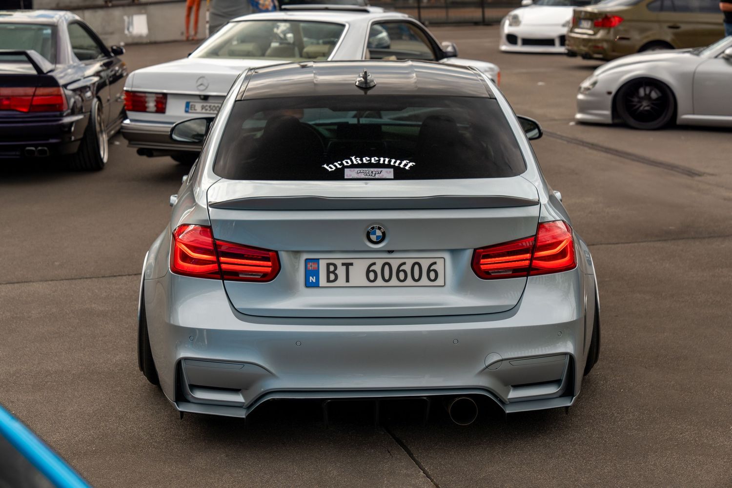 Silver BMW M4 rear view showing custom spoiler and taillights against parking lot setting.