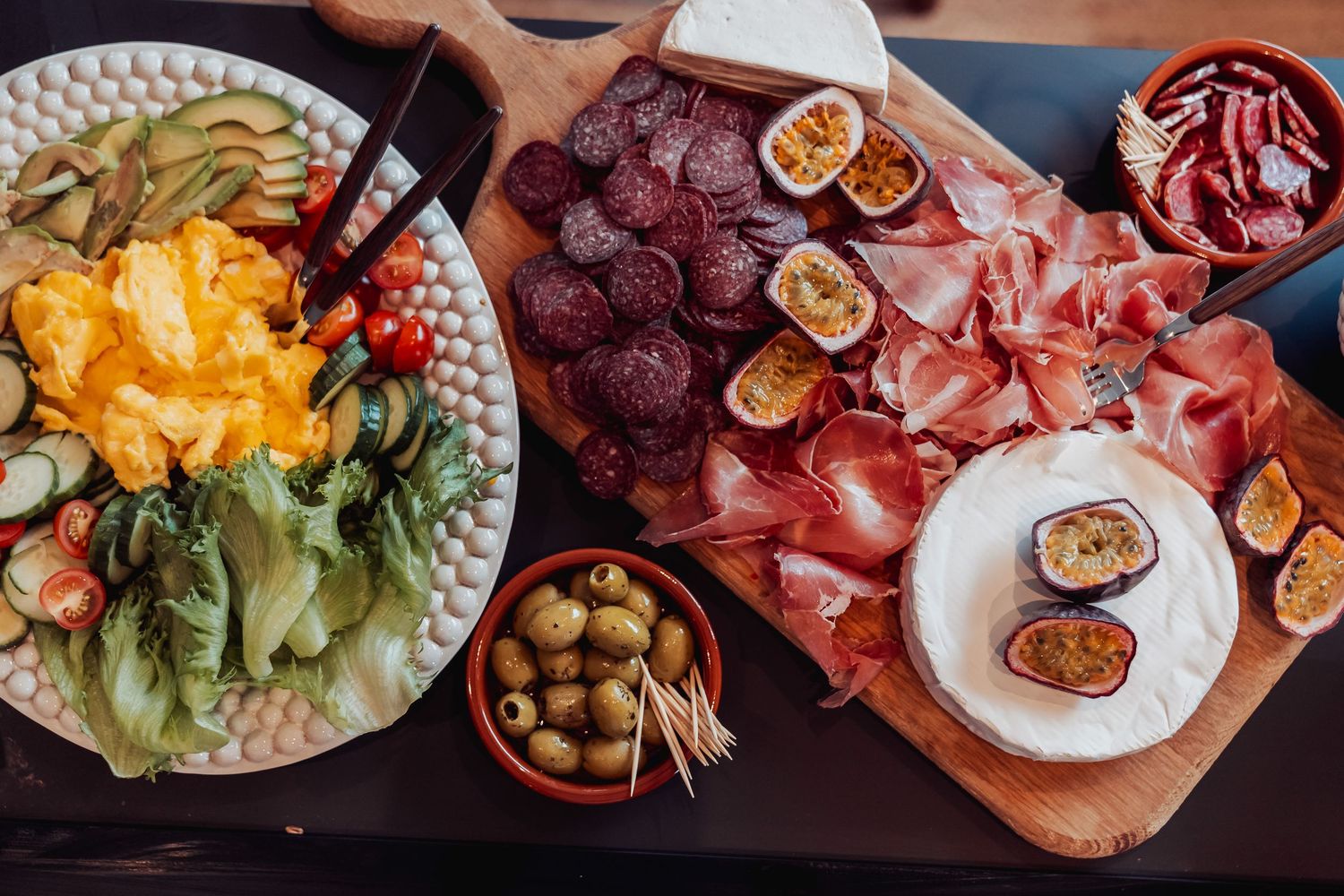 Colorful party spread featuring charcuterie, fresh salad, and antipasto on wooden serving boards.