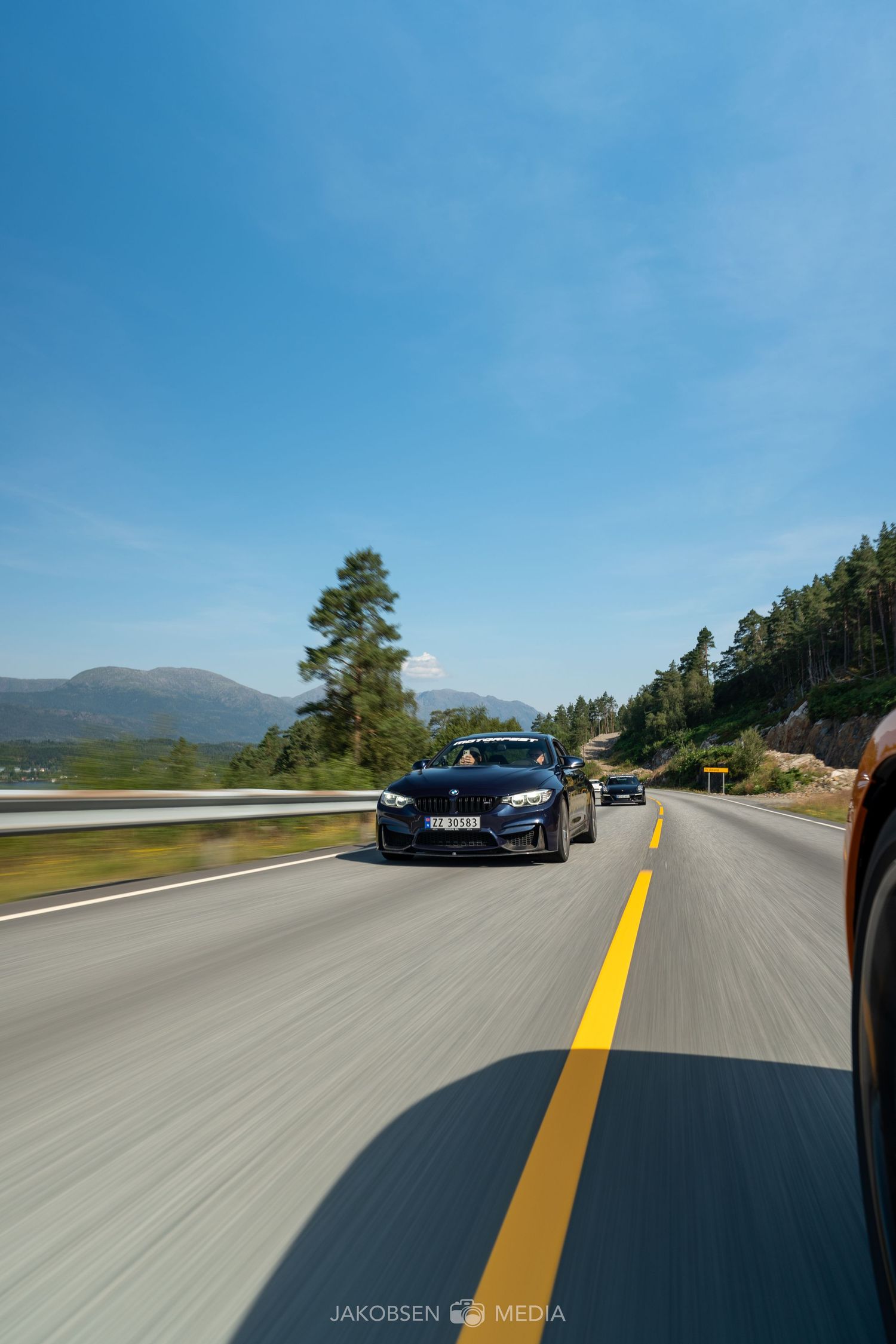 High-speed action shot of supercars racing down an empty mountain highway under clear blue skies.