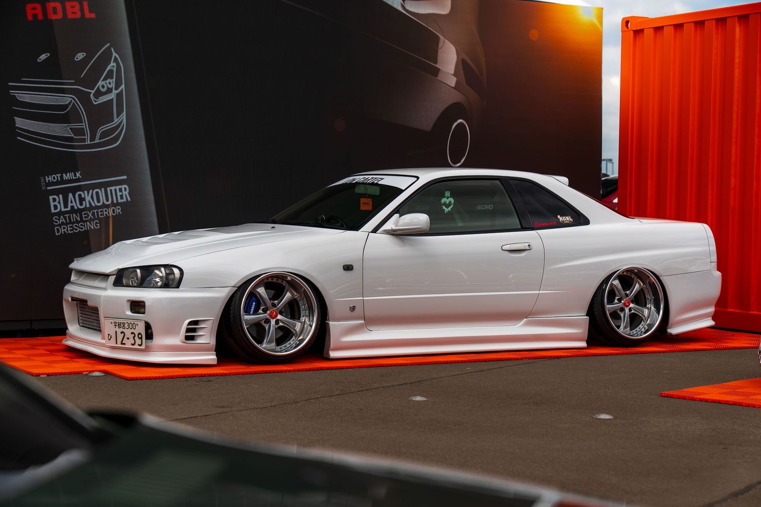 A lowered white Nissan Skyline GT-R with custom wheels displayed in a show setting.
