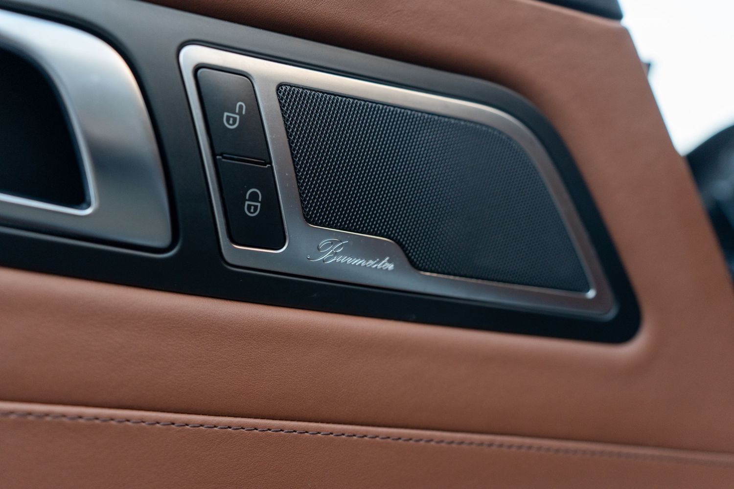Premium car audio speaker with Burmester branding mounted in brown leather door panel.