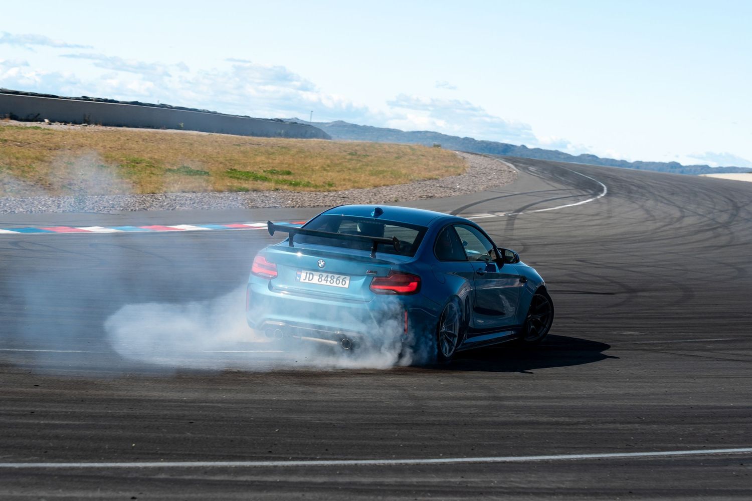 A blue BMW M3 drifts around a track creating smoke trails from its spinning tires during a performance demonstration.