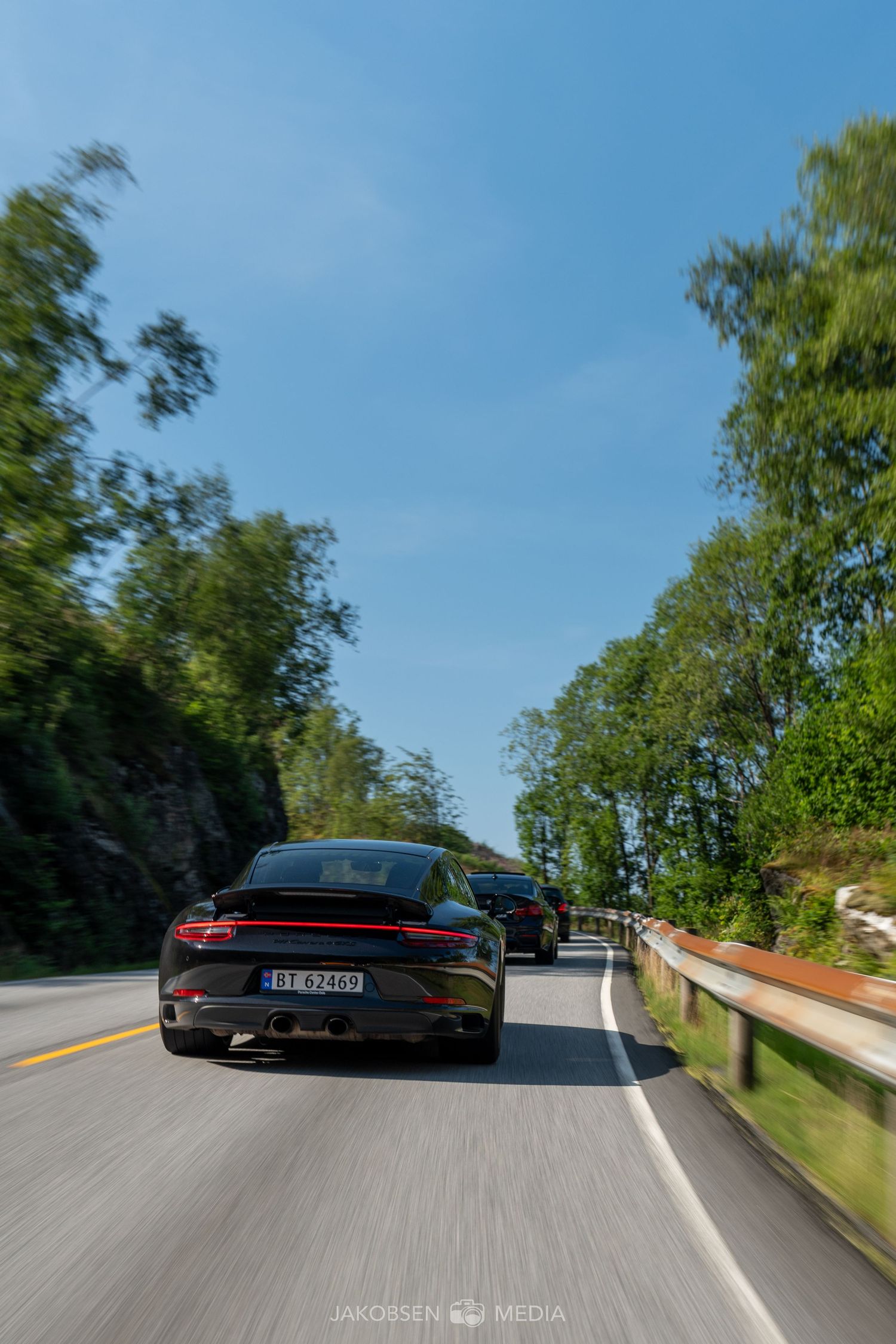 Black sports car photographed from behind while driving on a scenic mountain road.
