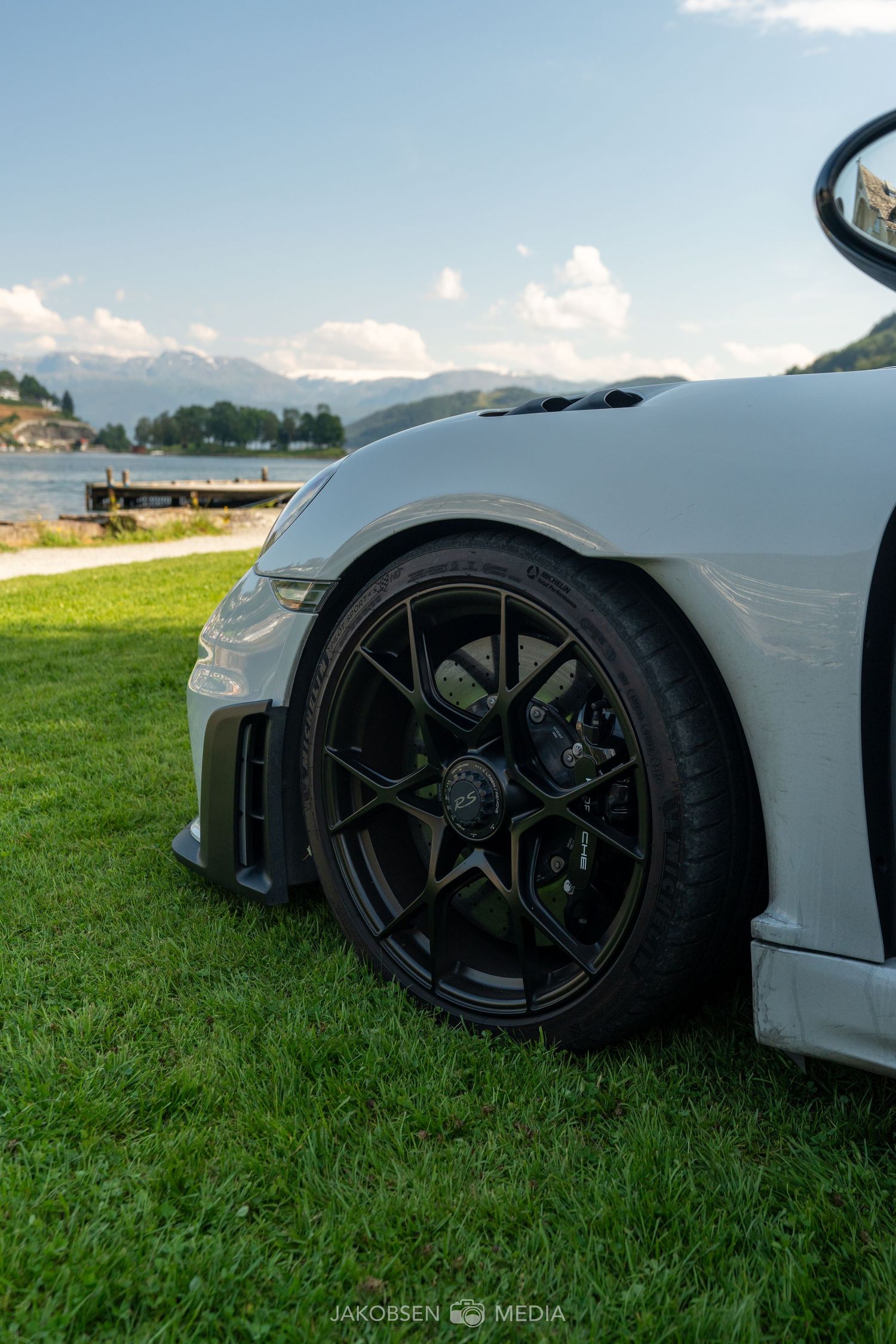 Close-up of black performance wheels and tires on luxury sports cars parked on grass.