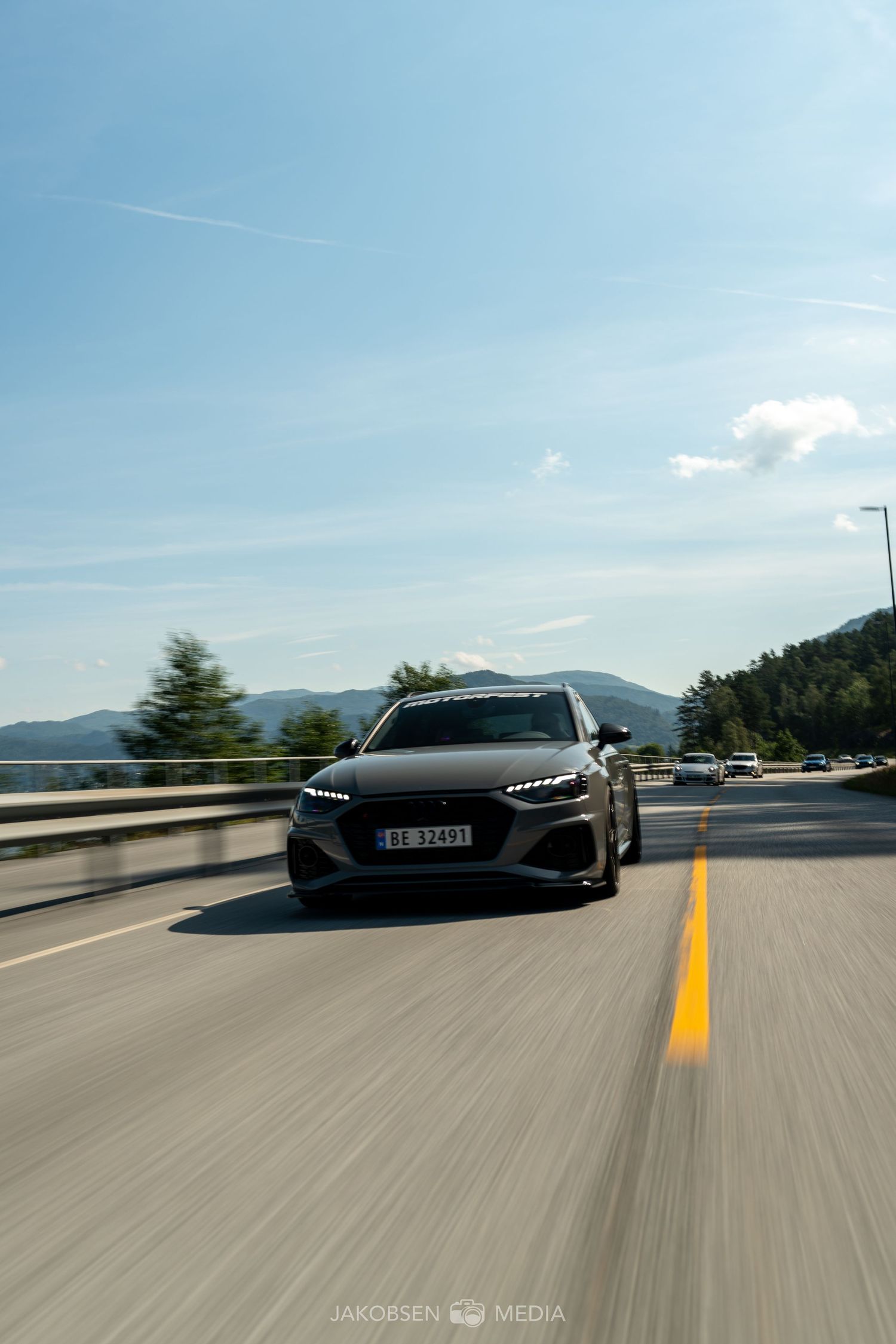 Black luxury sports car driving on highway with mountain scenery in background.