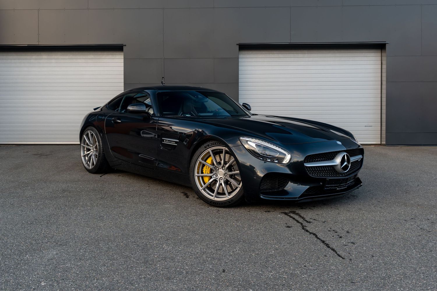 Black Mercedes-AMG GT sports car parked in front of industrial garage doors.