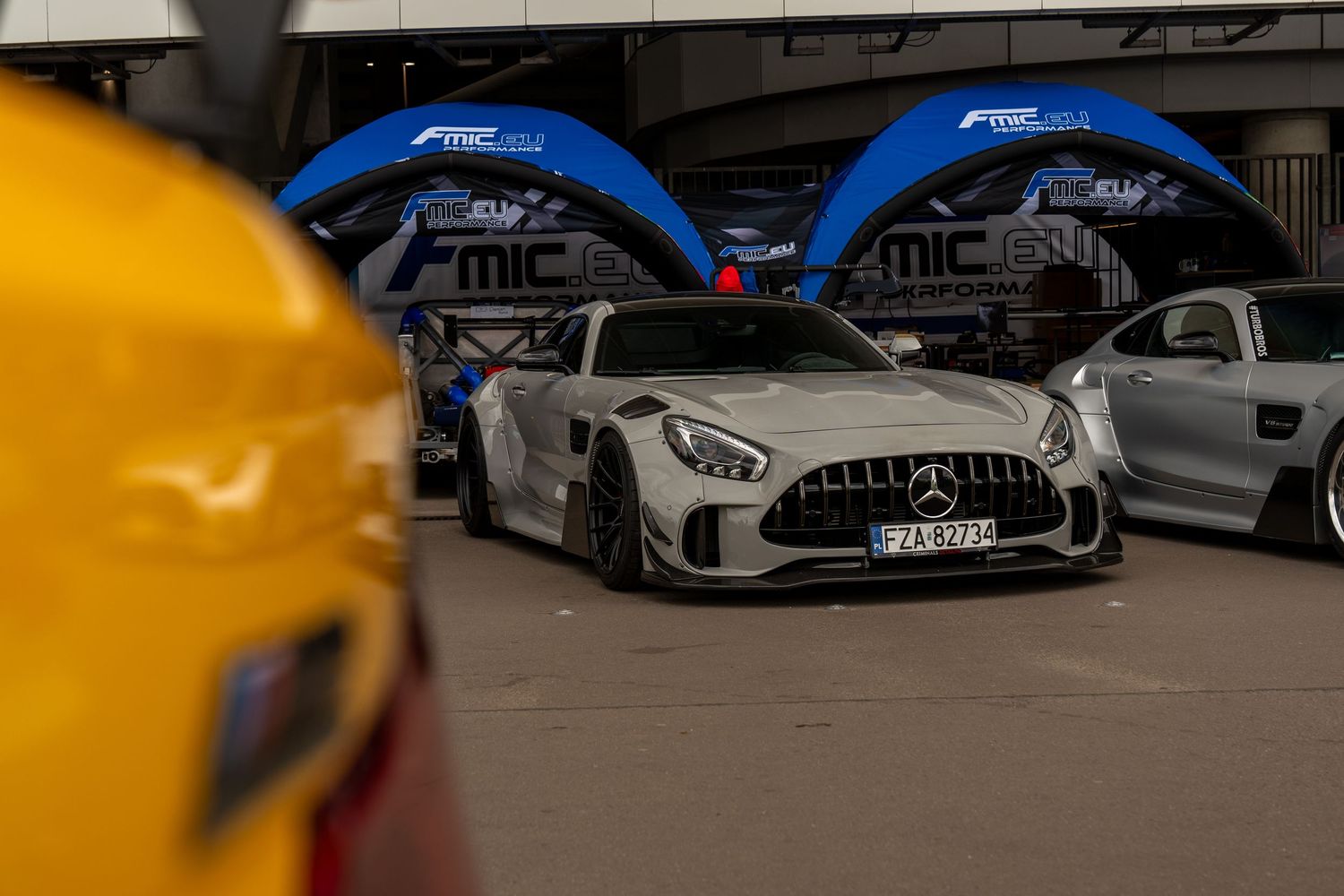 Silver Mercedes-AMG GT with aggressive body kit parked under blue event tents.