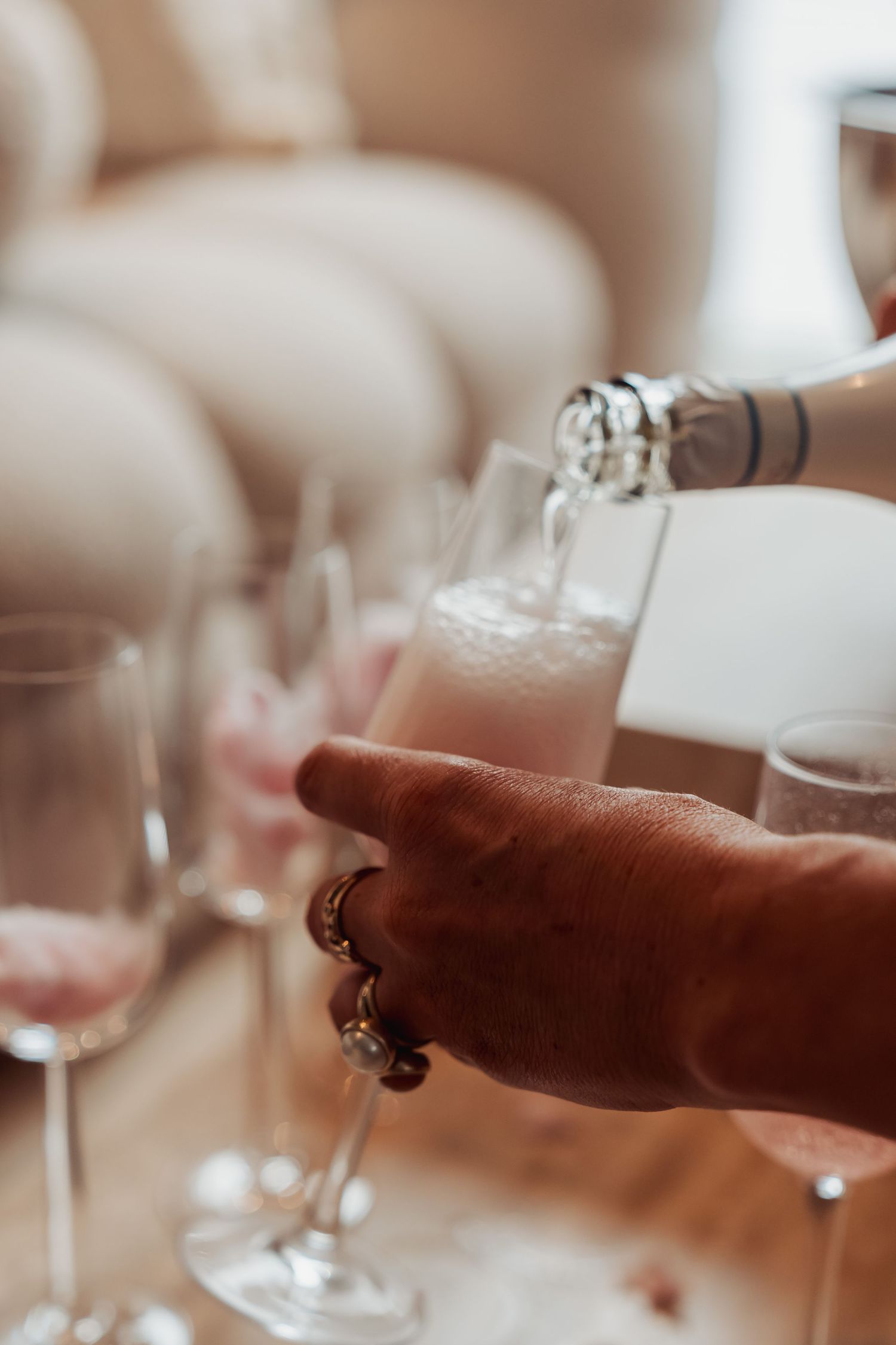 Closeup of champagne being poured into a glass with rings visible on the pourer's hand.