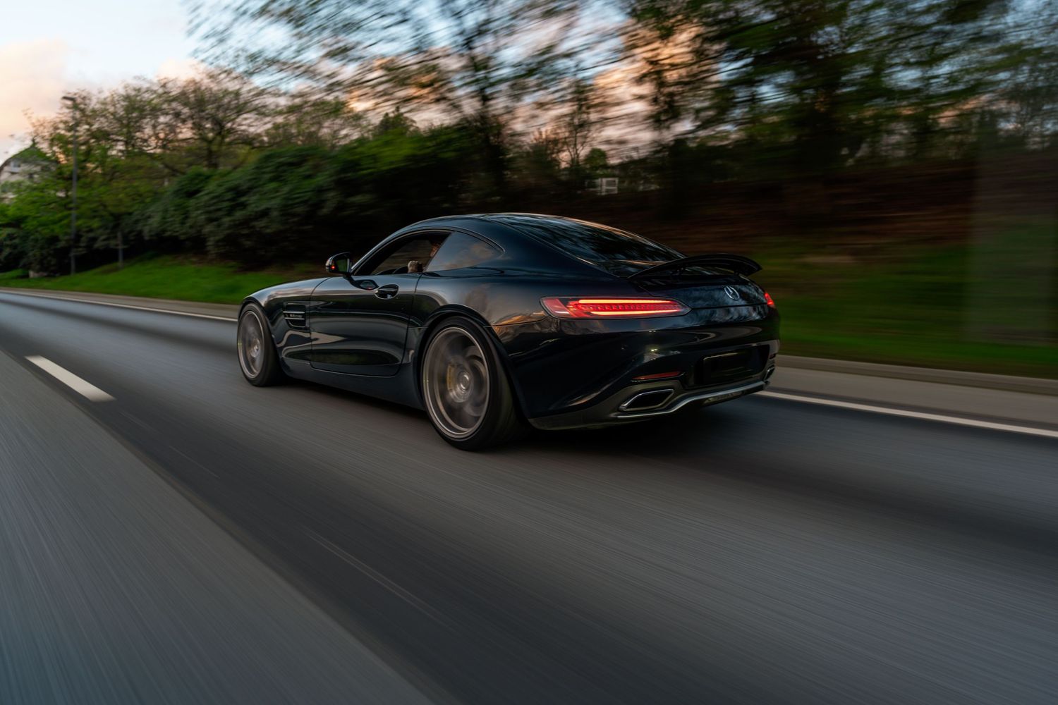 Black Mercedes AMG GT photographed from behind while driving on a scenic road.