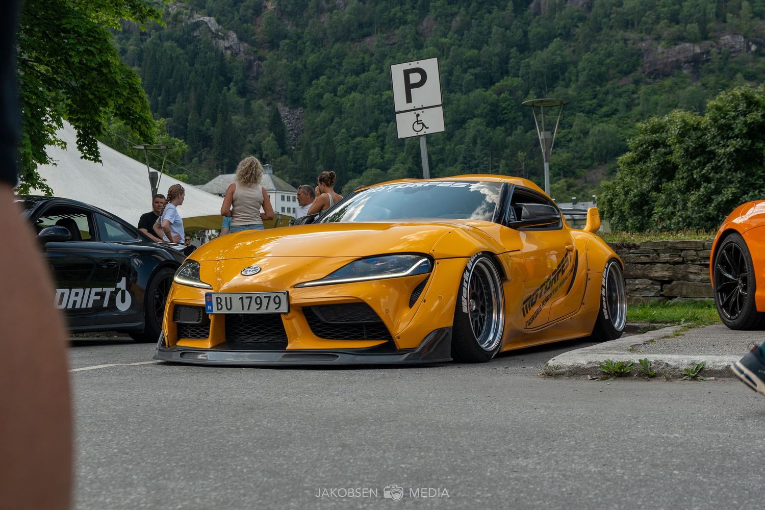 Row of exotic sports cars including yellow and silver models parked against mountain backdrop.