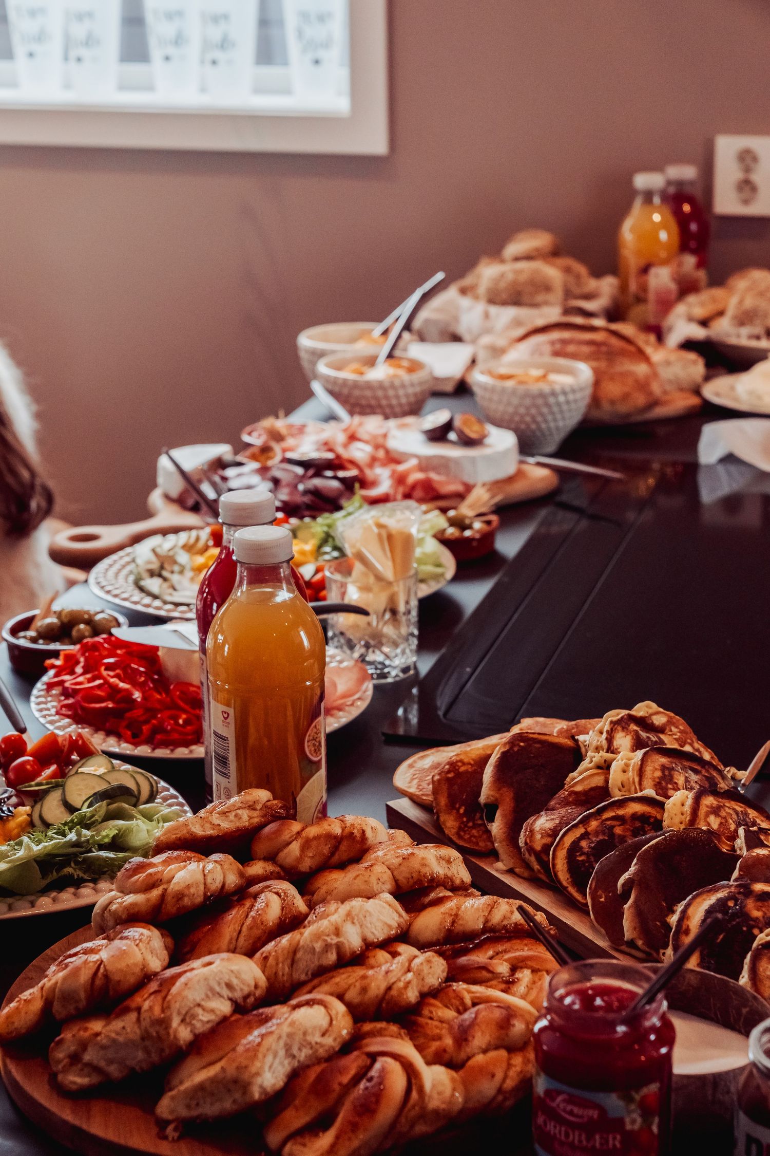A festive brunch spread with pastries, meats, cheeses and orange juice bottles on a dark table.