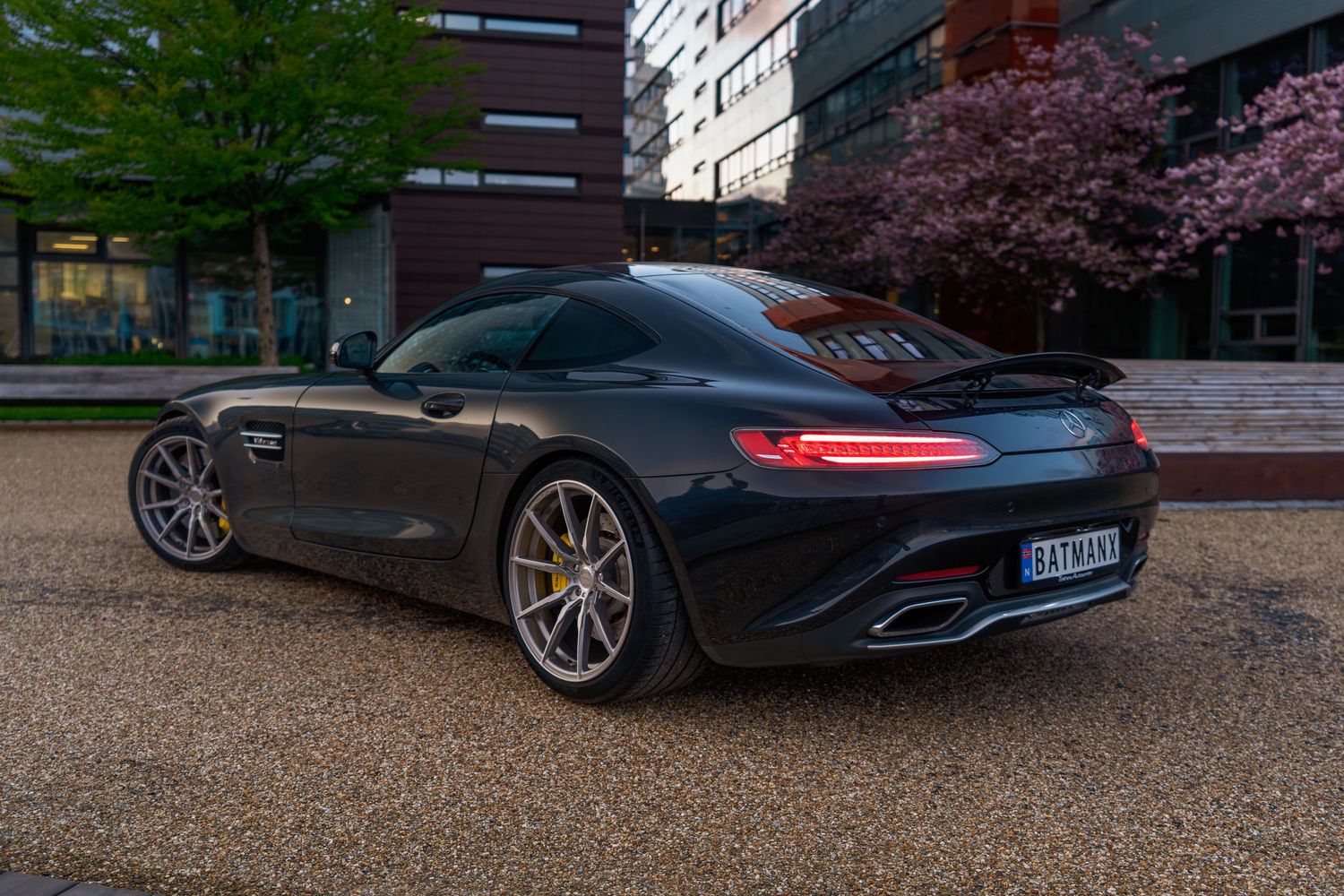 Mercedes AMG GT parked in front of modern architecture with cherry blossoms in background.