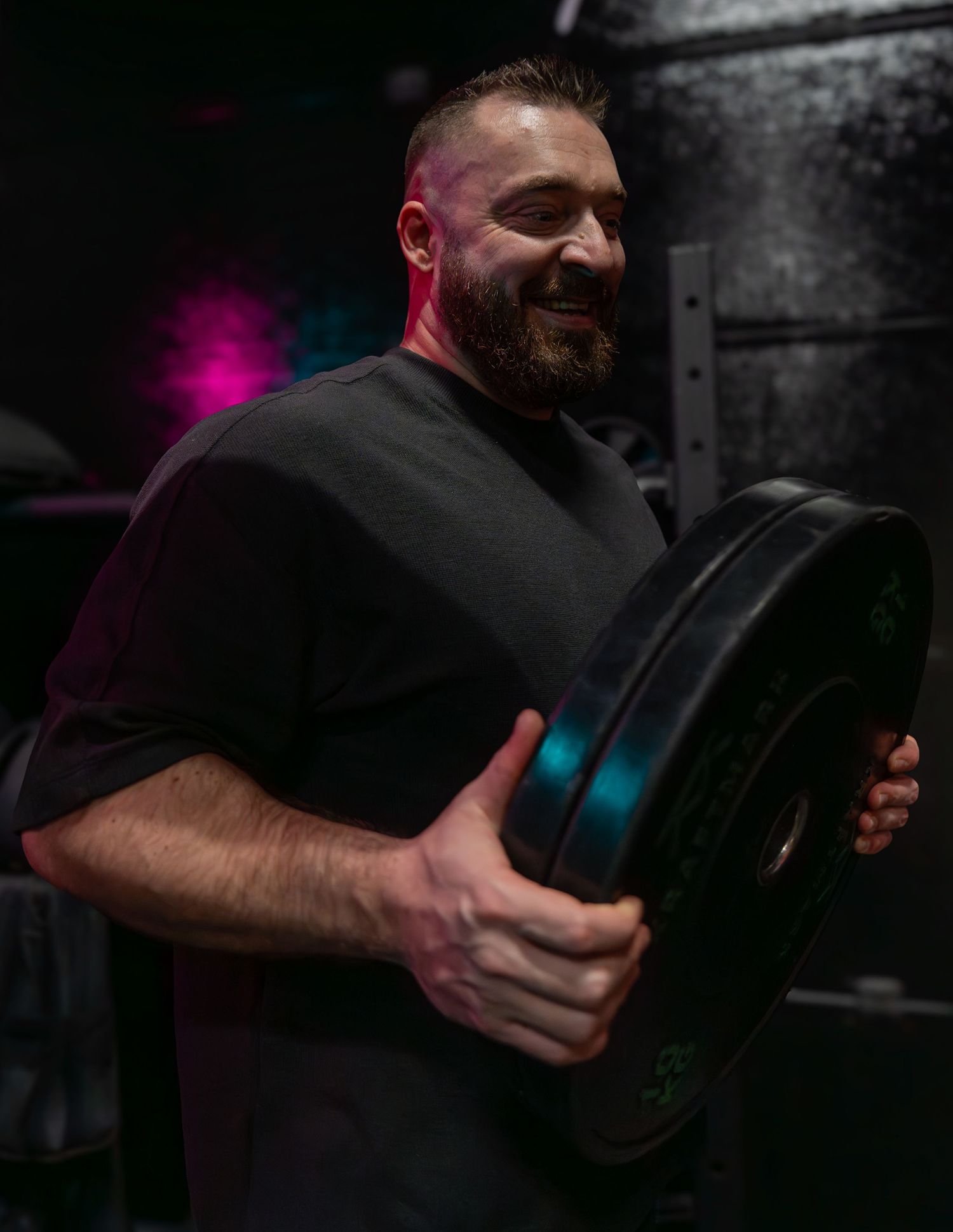 Strong person holding weight plate while working out in dimly lit gym setting.