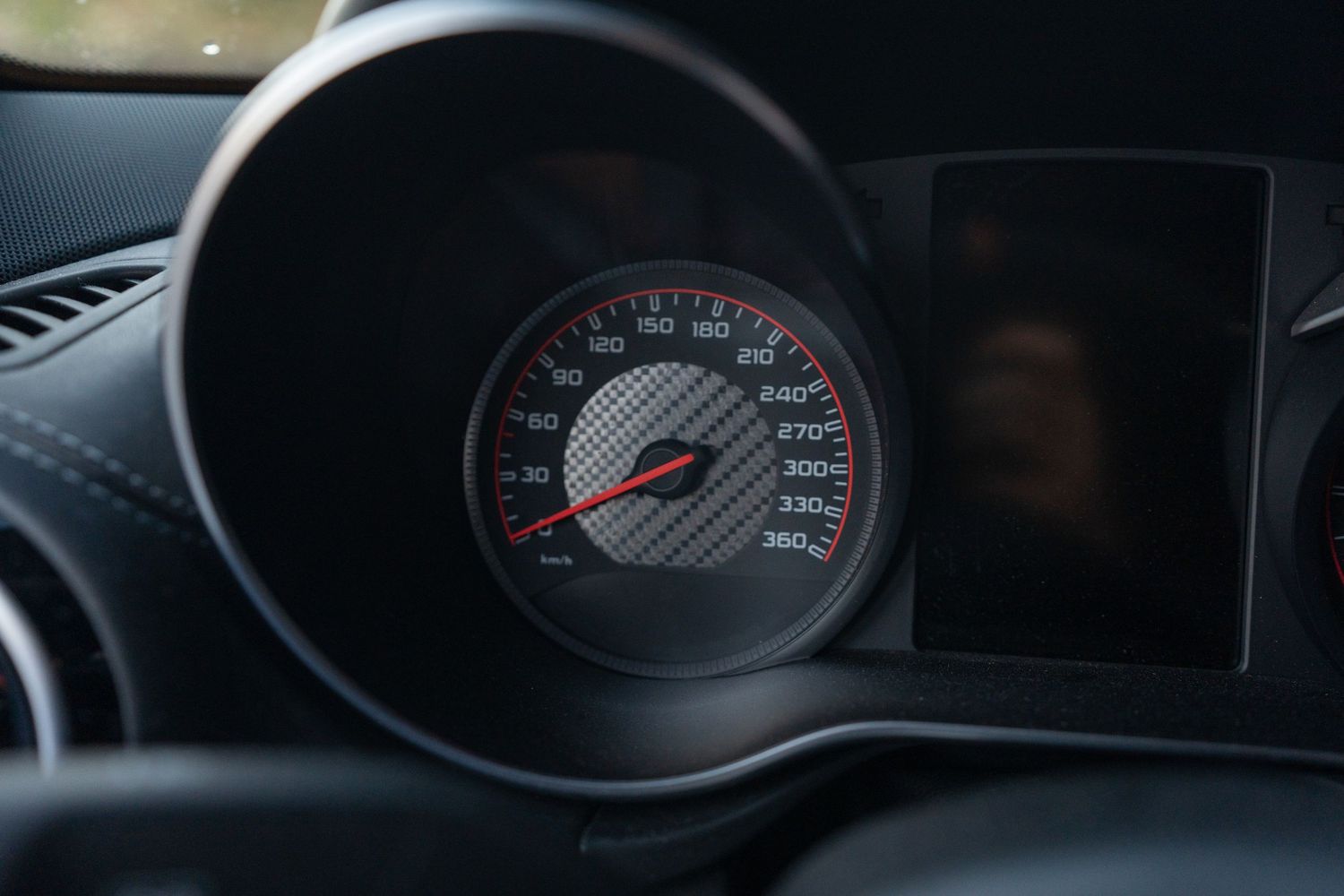 Round automotive gauge cluster showing speedometer with red accents and digital display.