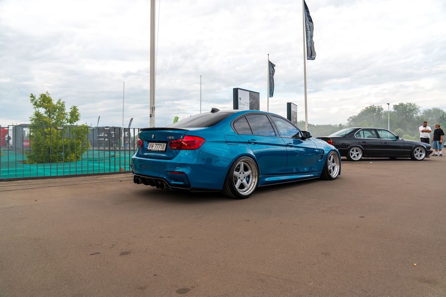 Lowered blue BMW M3 with custom wheels parked at an outdoor event venue.
