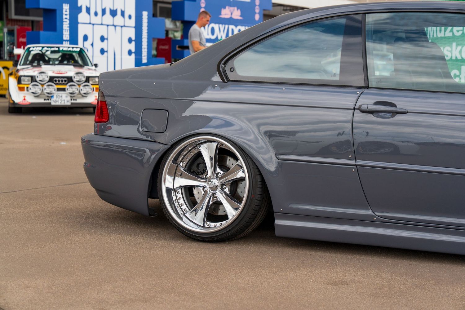 Gray BMW sedan with custom chrome wheels and lowered suspension parked at a car show.