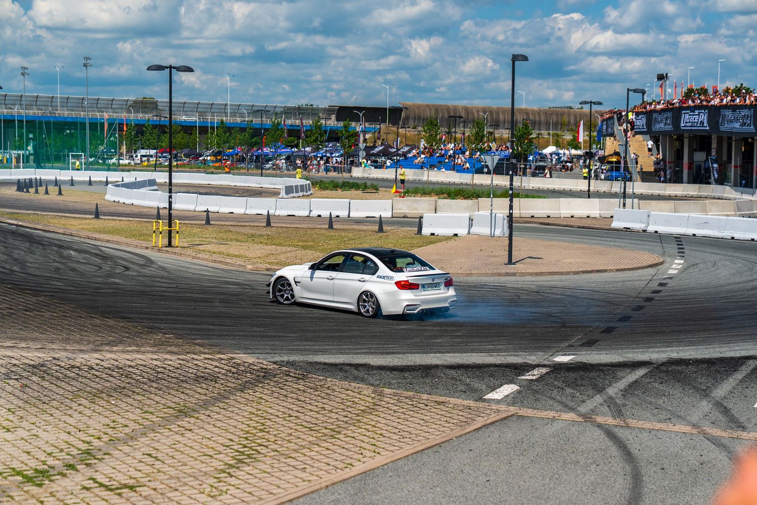 White BMW drifting around a corner on a track with spectator areas and barriers visible.