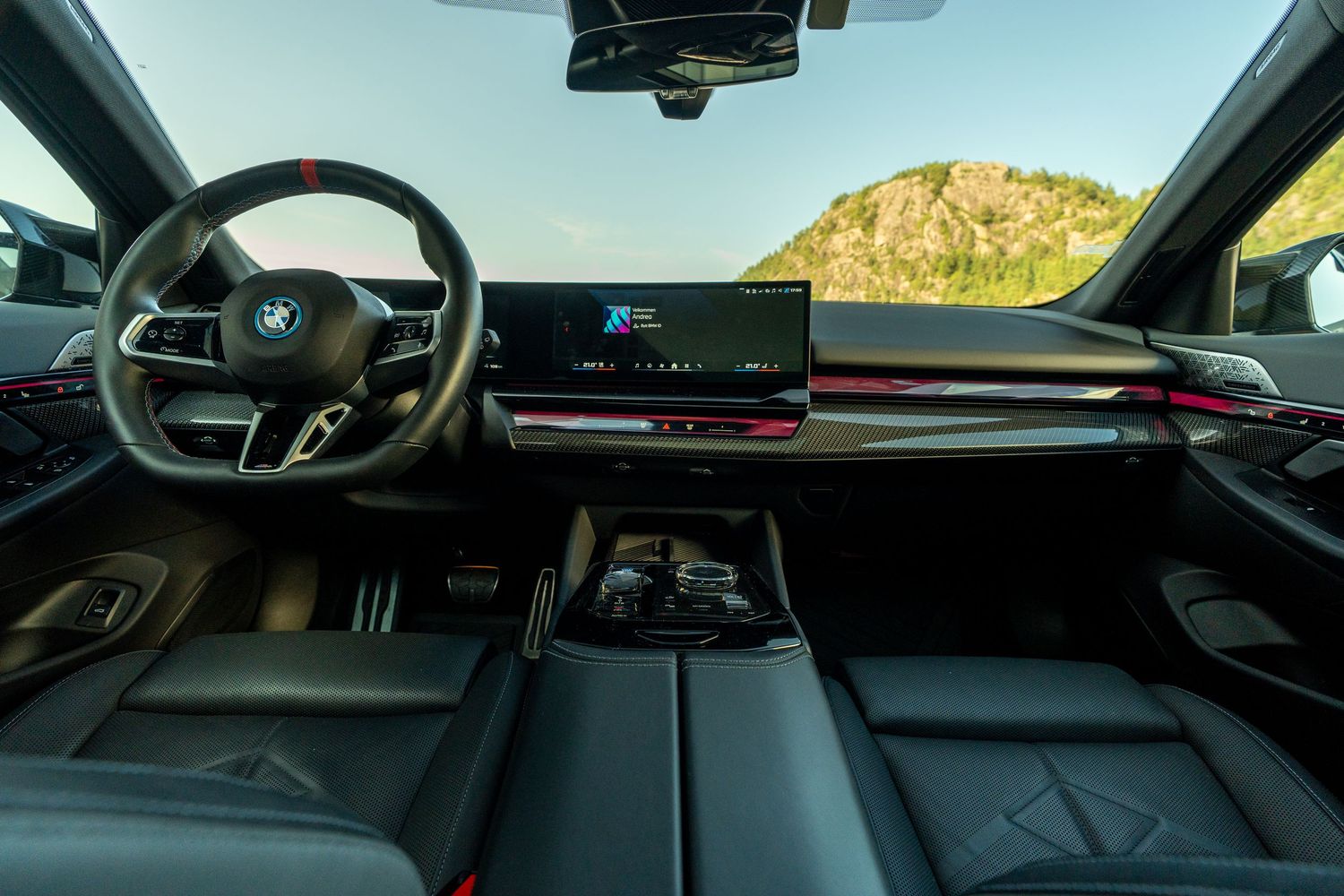 BMW dashboard display showing curved digital instrument panel and infotainment screen with scenic mountain view outside.