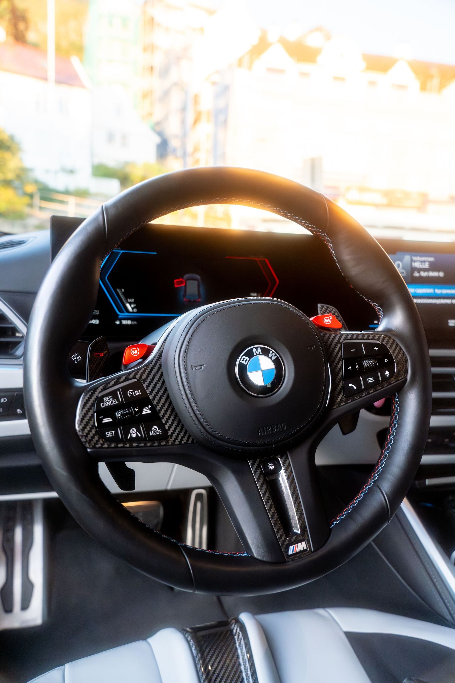 Close-up view of a modern BMW steering wheel showing digital dashboard displays and controls.