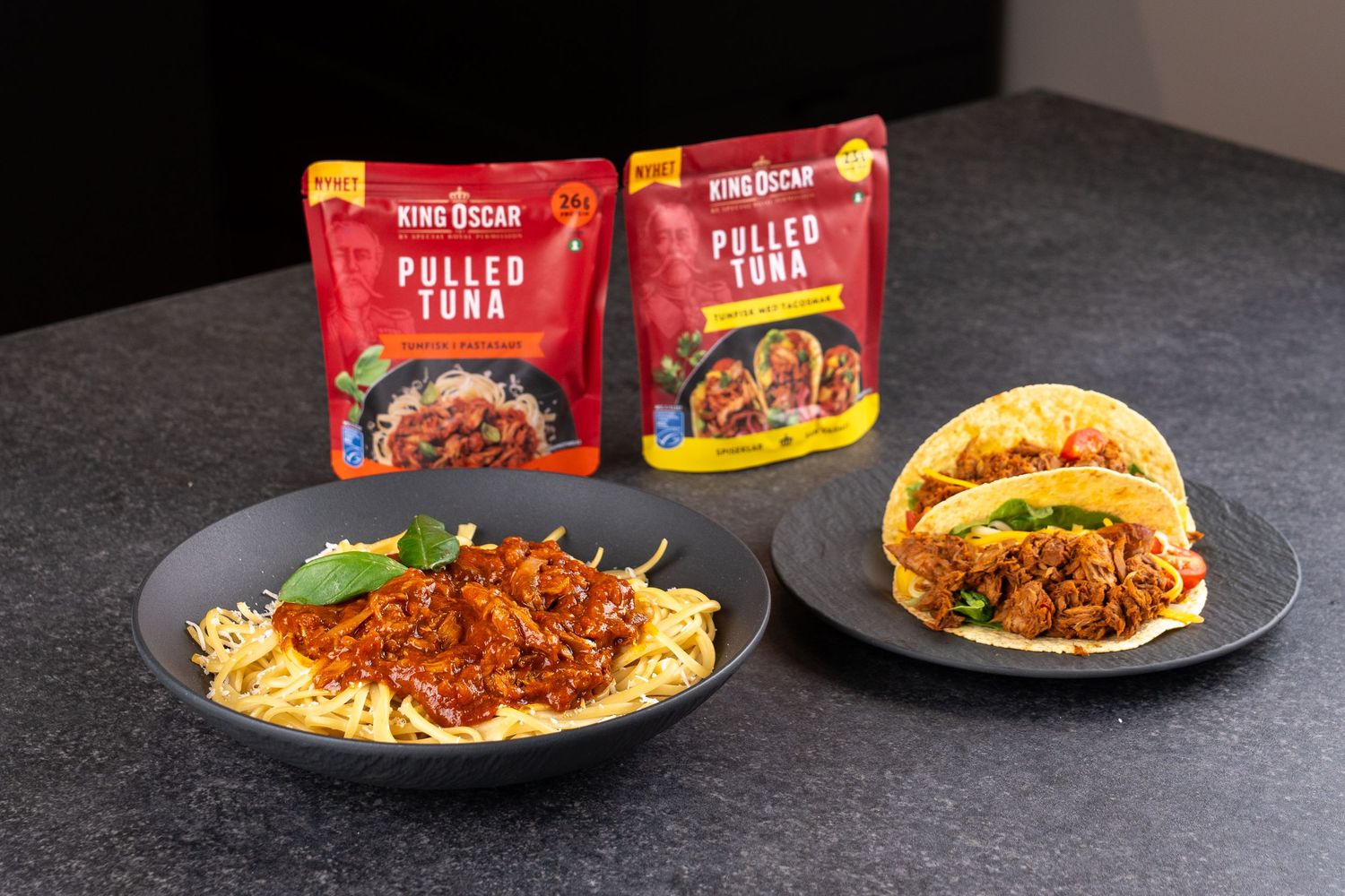 King Oscar Pulled Tuna pouches beside a bowl of spaghetti with tuna sauce and basil and a plate of pulled tuna tacos.
