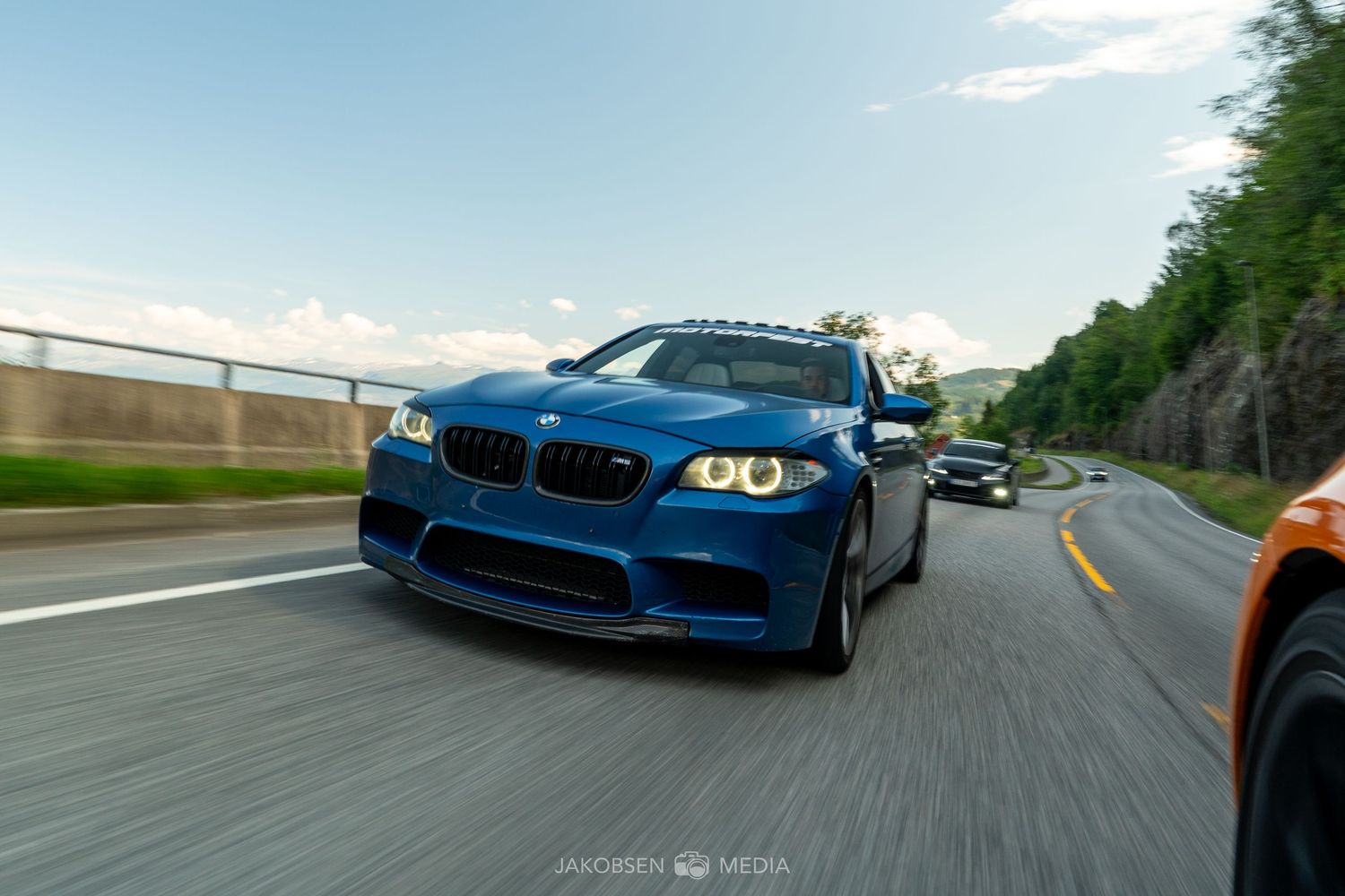 Blue BMW M5 speeds down a mountain road with motion blur effect.