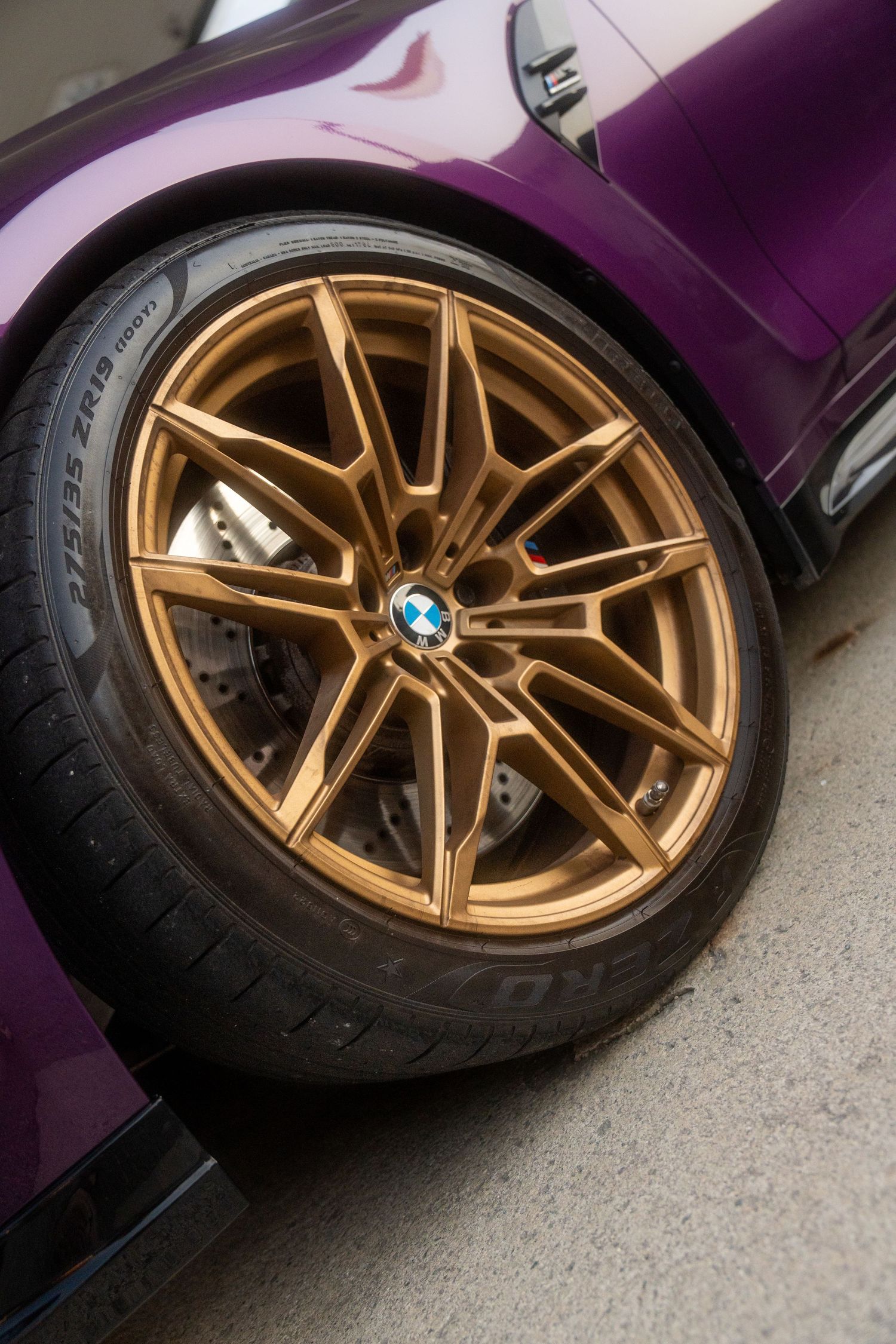 Gold alloy wheel with BMW logo on purple car showing premium brake setup and low profile tire.