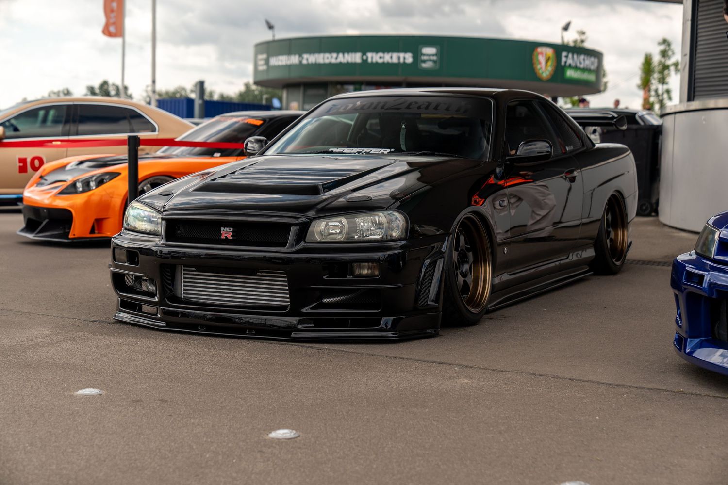 Black modified Nissan Skyline GT-R R34 with aftermarket wheels and body kit at a car show.