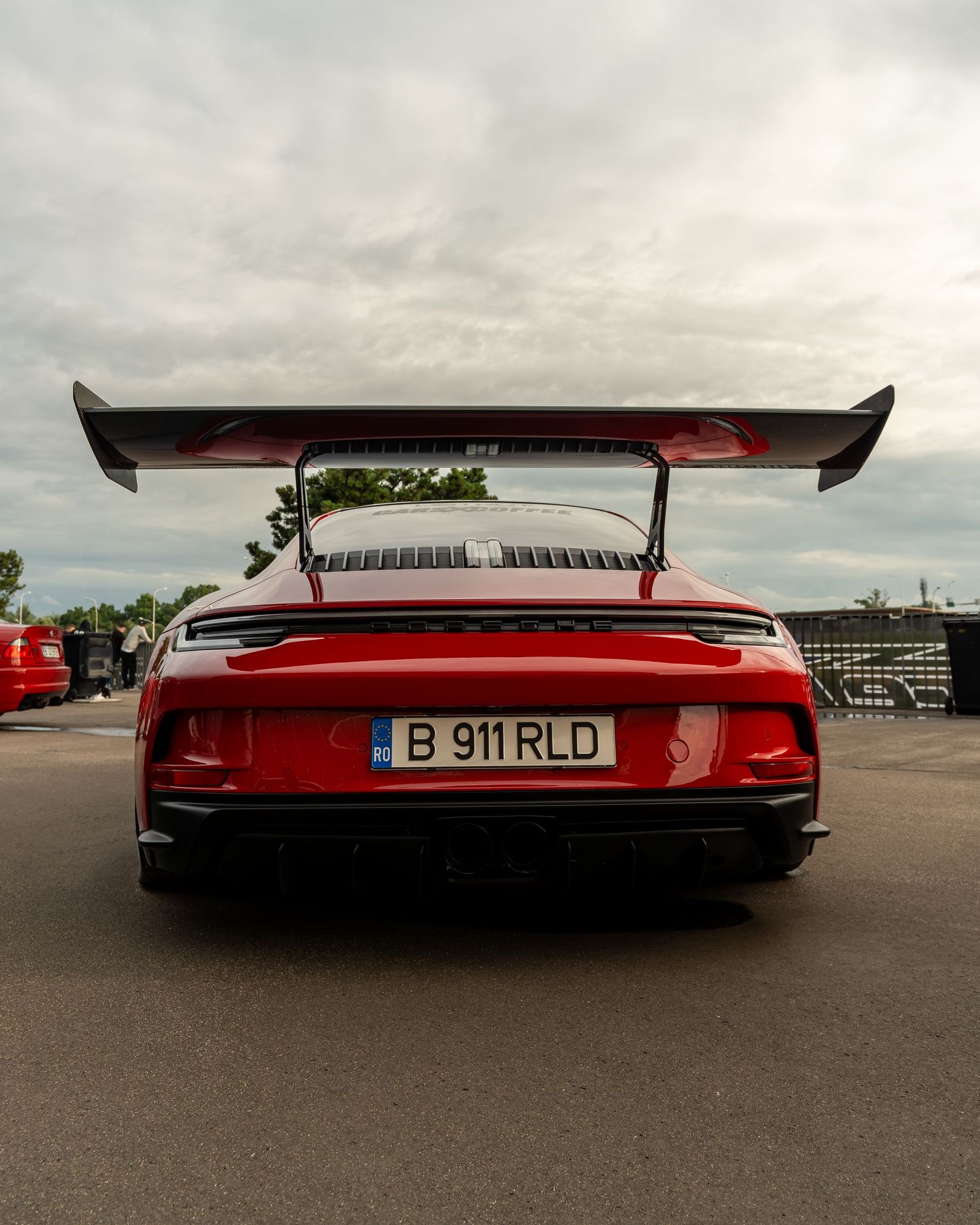 Rear view of a red Porsche 911 GT3 with large rear wing parked outdoors under cloudy skies.