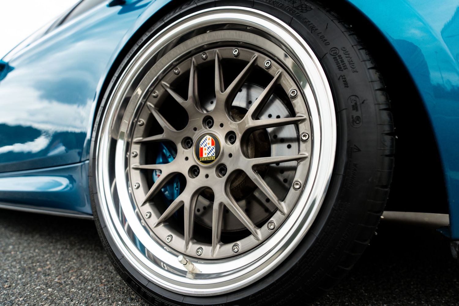 Detail shot of multi-spoke HRE wheel with chrome lip on blue BMW M3.