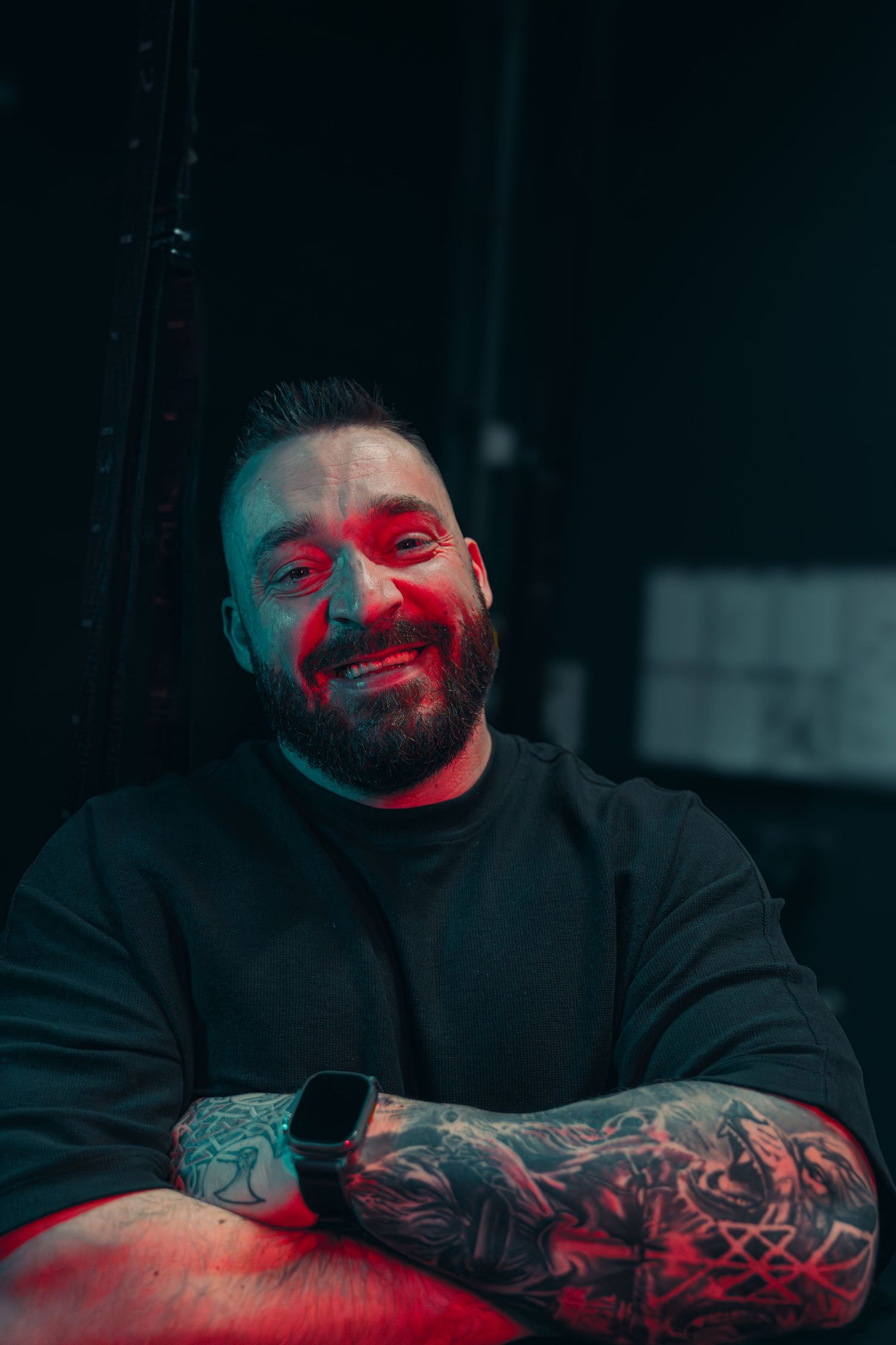 Portrait of a tattooed person illuminated by red lighting in a dark setting.