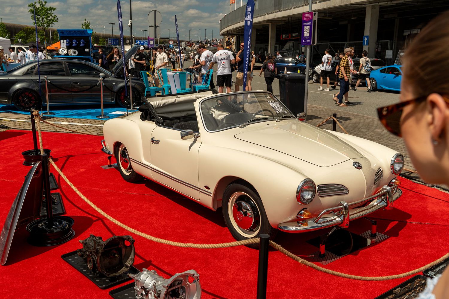 Classic cream-colored Volkswagen Karmann Ghia convertible displayed on red carpet at car show.