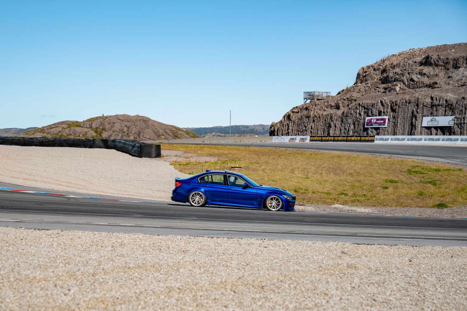 Blue sports car speeds around a curved racetrack with mountains and desert landscape in the background.