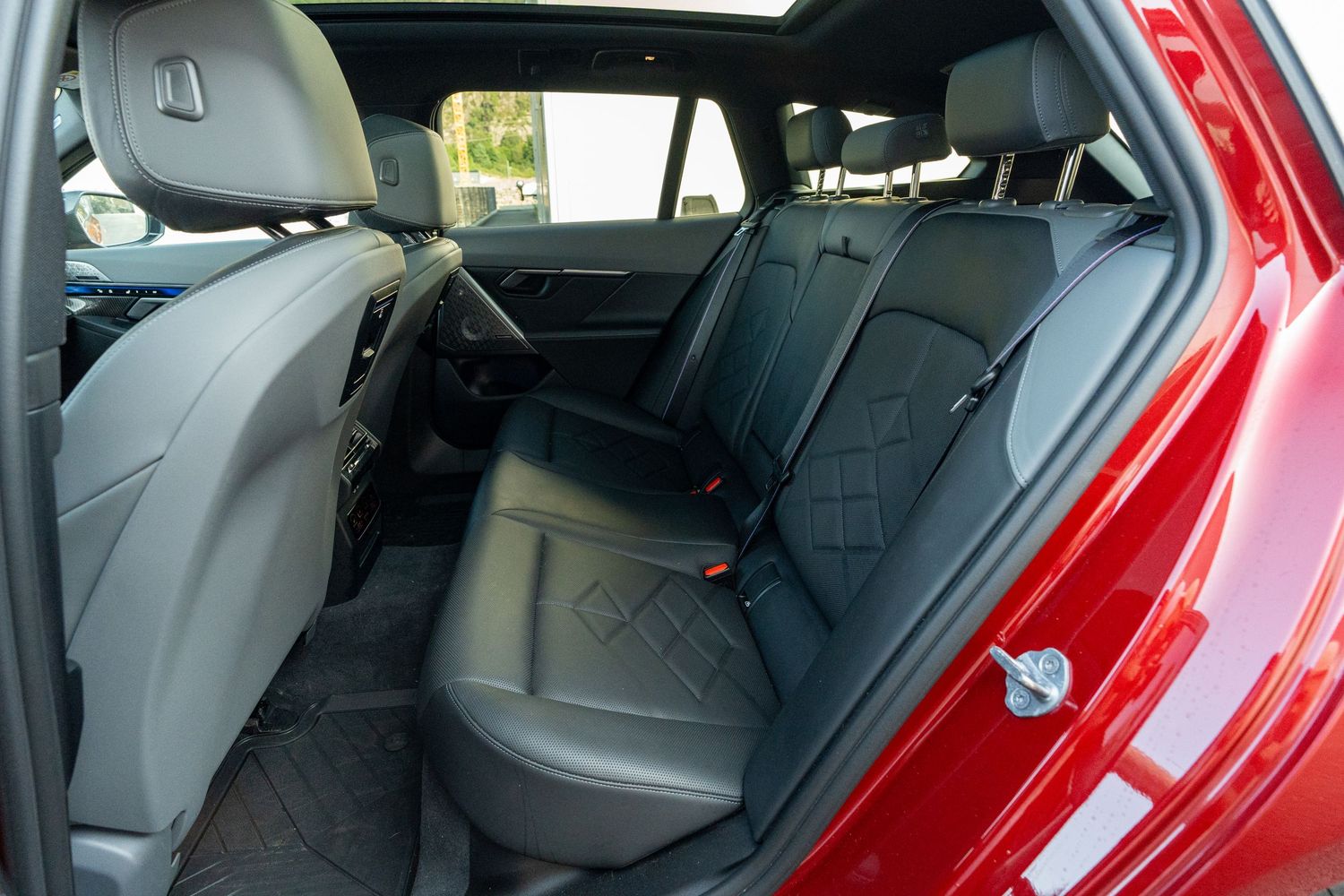 Spacious rear seats of a red luxury car with black leather upholstery and diamond stitching.